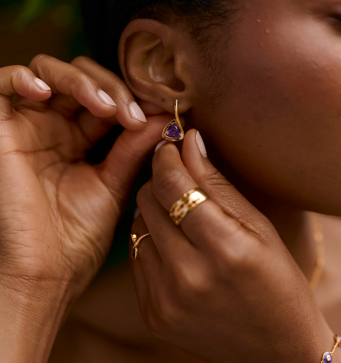 Close-up of a person wearing Samya Earrings with purple amethyst and gold setting