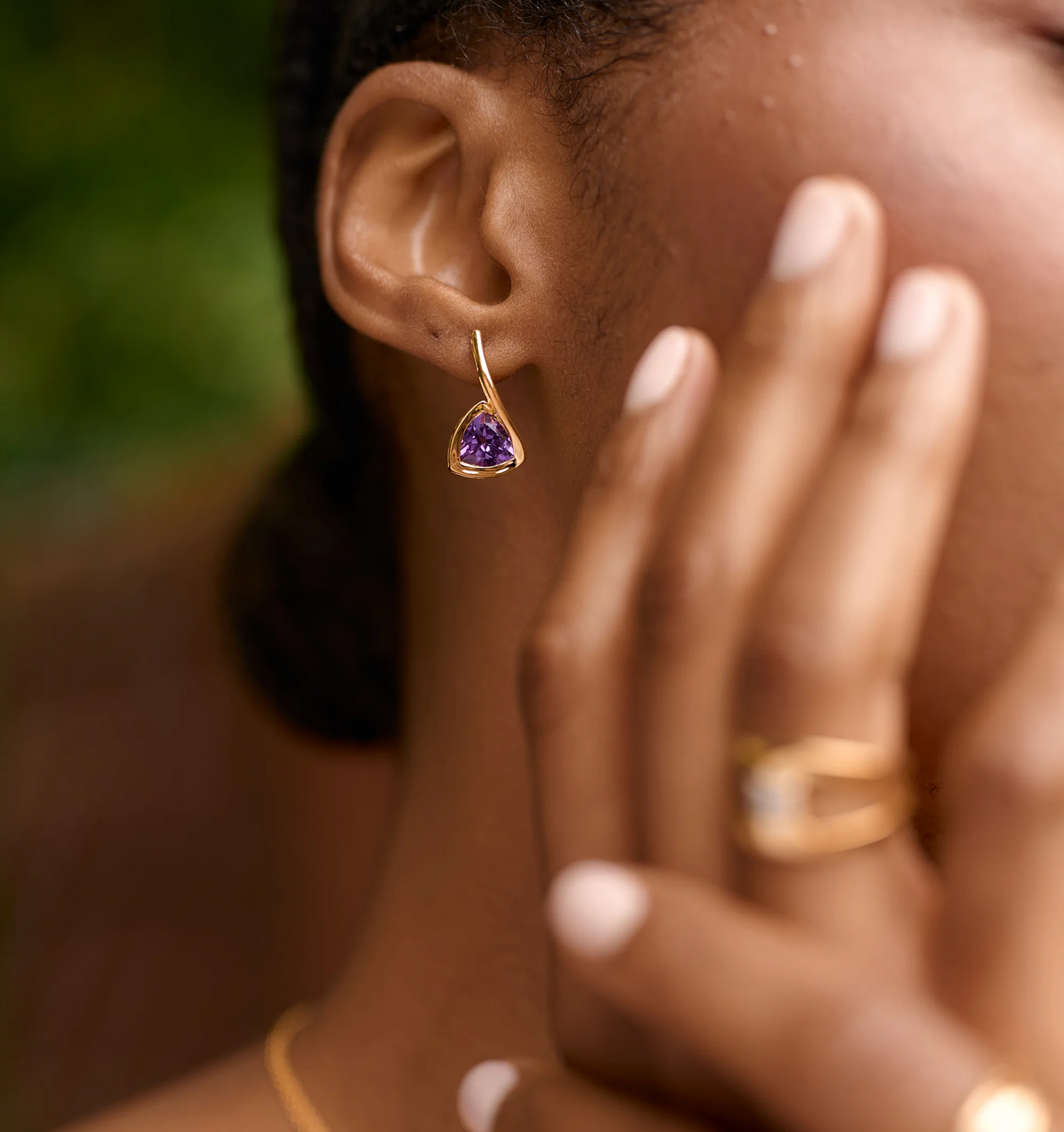 Close-up of Samya Earrings featuring a purple amethyst stone set in gold on a woman's ear