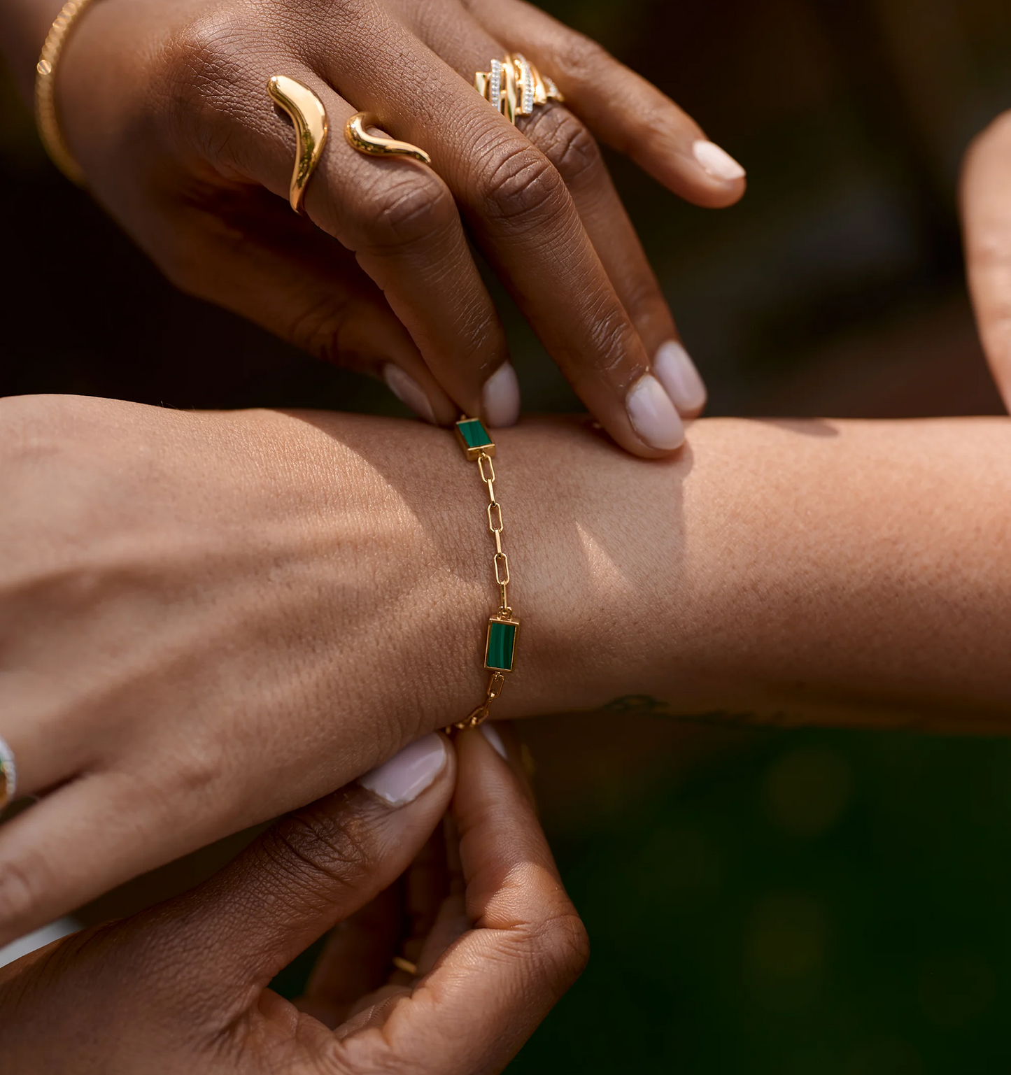 Close-up of hands wearing a delicate gold Mann Bracelet with green rectangular stones