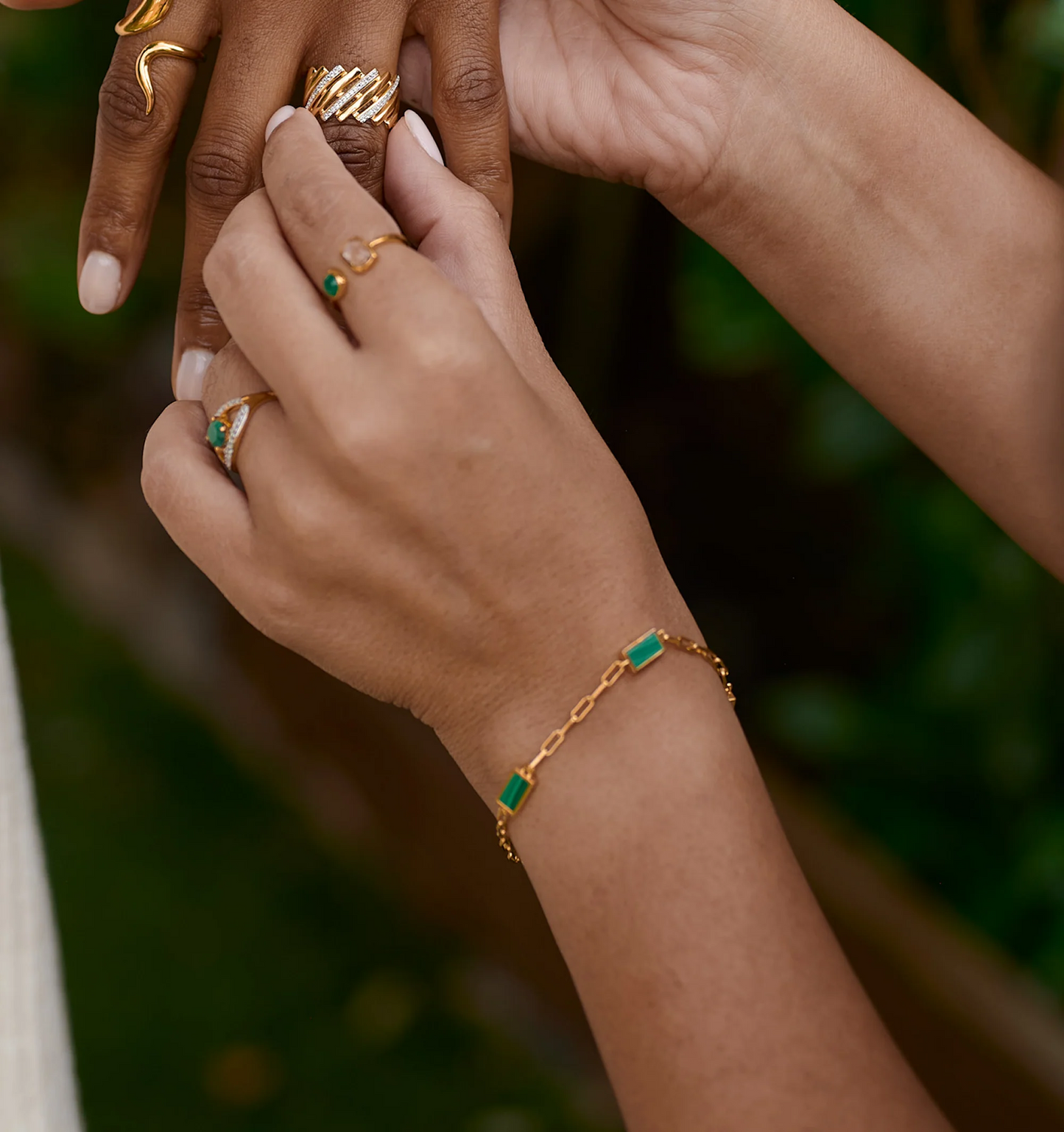 Gold Mann Bracelet with green stones on wrist, styled with gold rings on hand