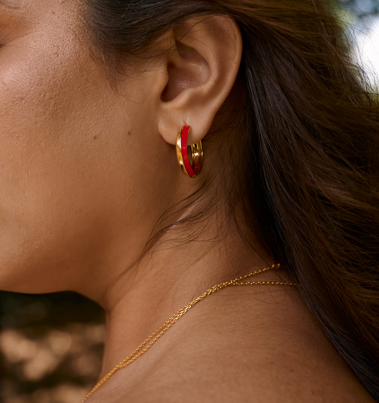 Close-up of ear wearing Ravya Ring hoop earring in gold and red enamel