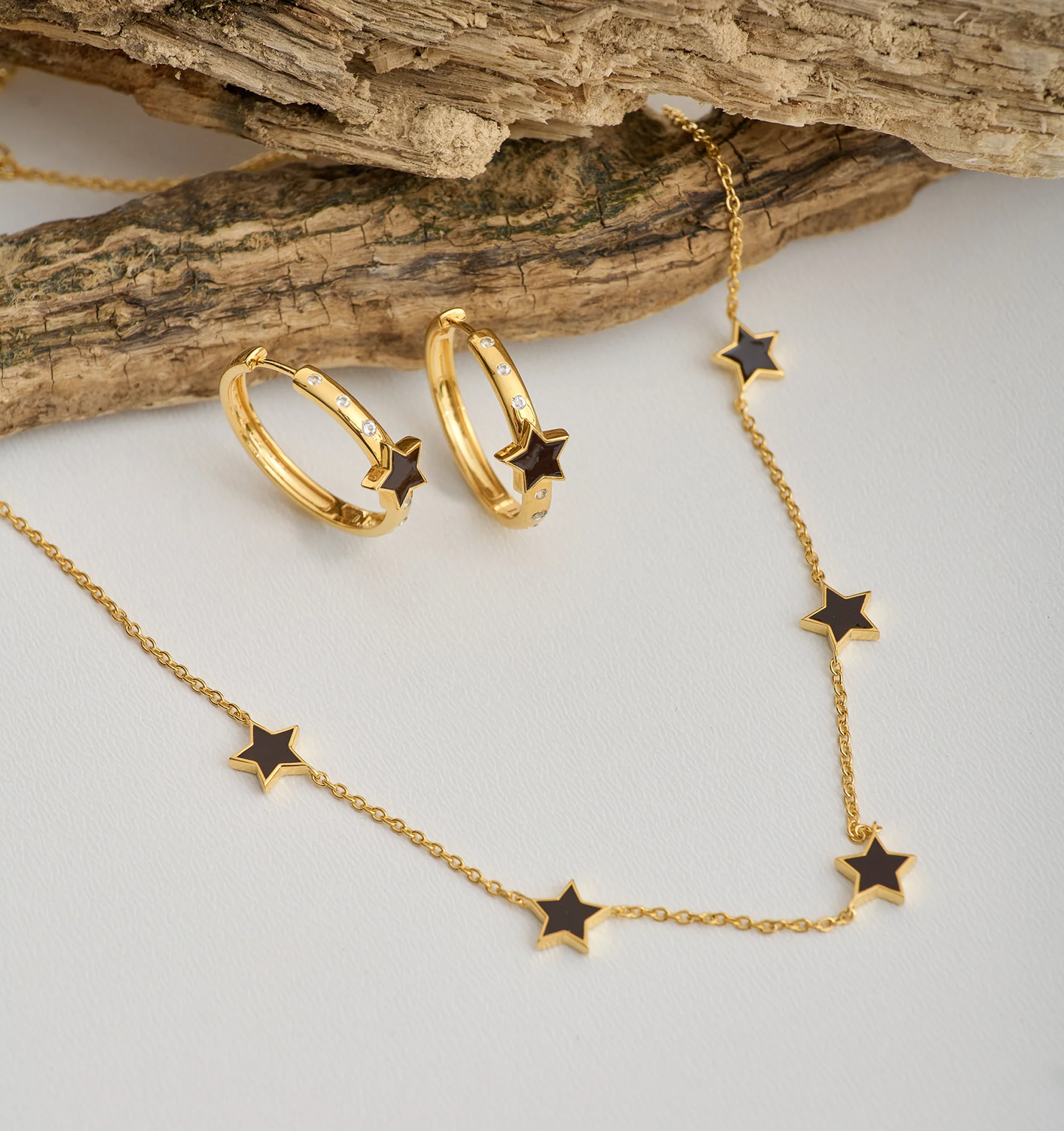 Tara Nova Hoop gold earrings with star design and matching star necklace on rustic wood background