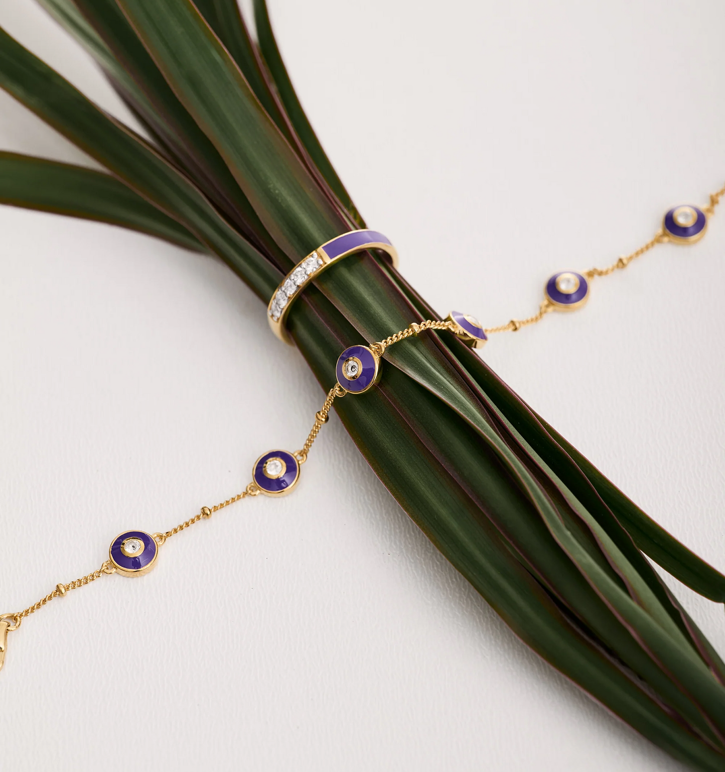 Viraah Bracelet with violet enamel and white topaz on gold chain around green leaves