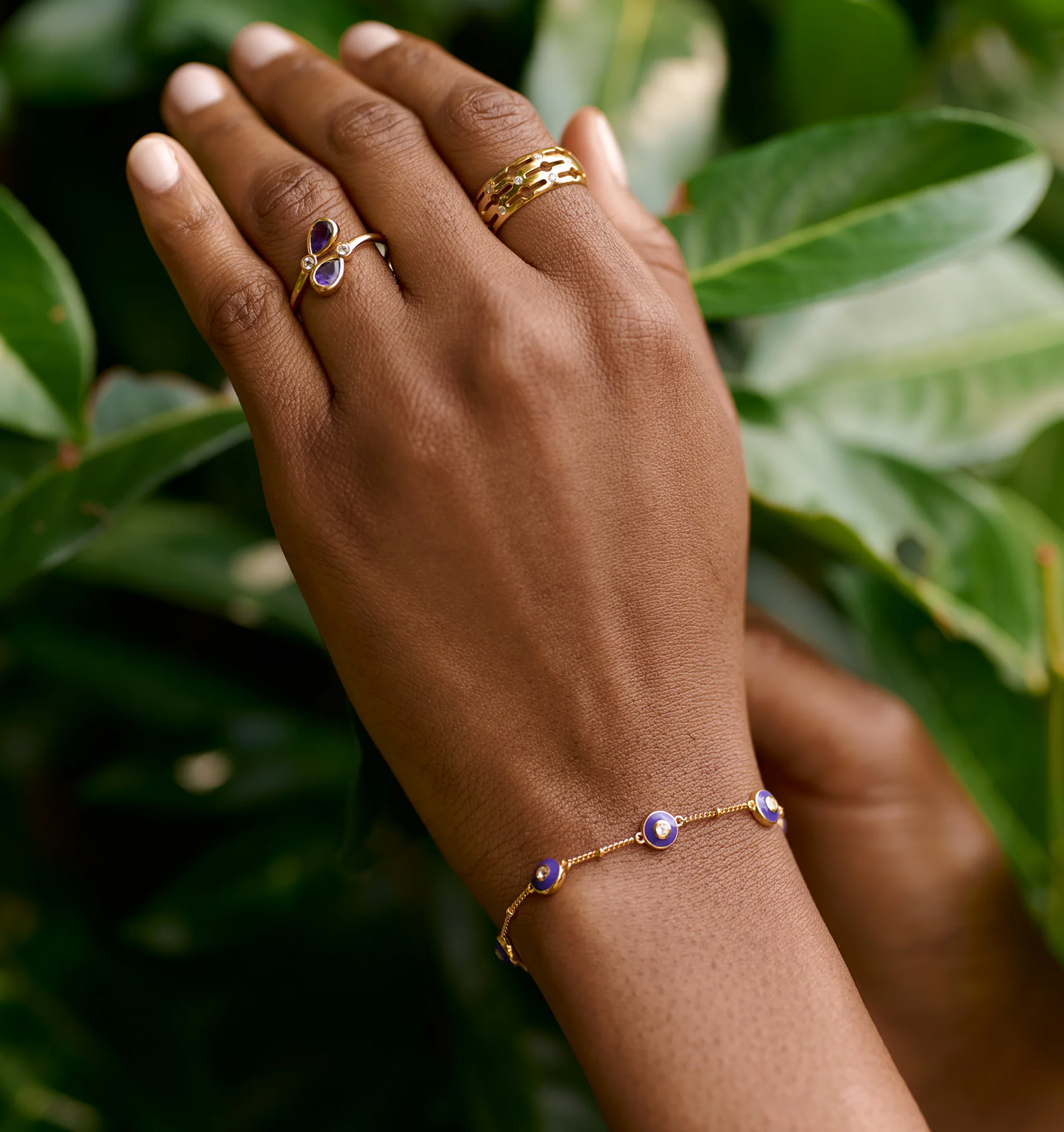 Viraah Bracelet with violet enamel and white topaz on wrist against green leaves background