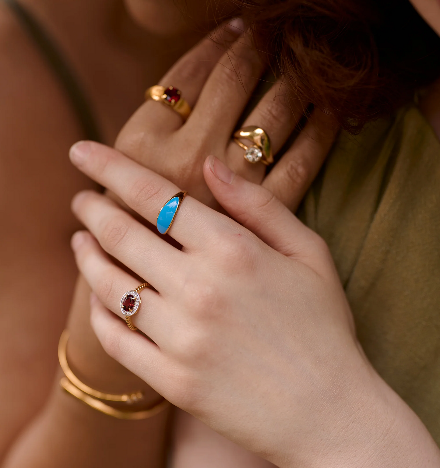 Close-up of hands wearing Neelra Ring with blue stone and gold bands inspired by water shapes