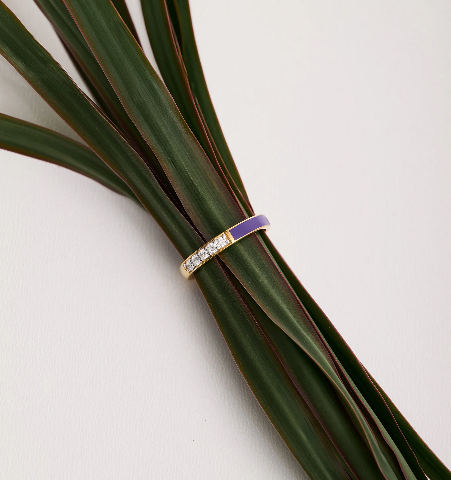 Pancha Ring gold band with purple arc and diamonds on green leaves background