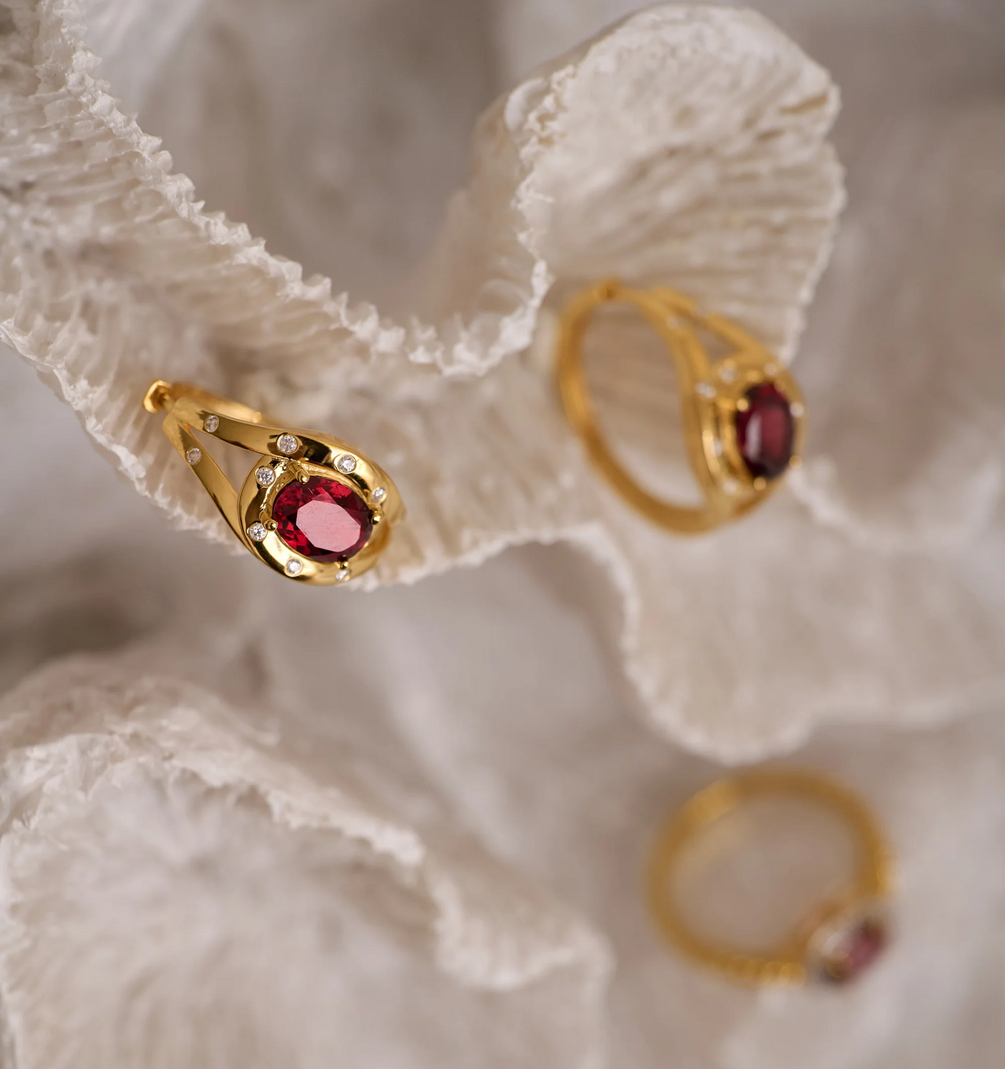Gold Ruvya Hoops earrings with garnet and white zircon accents on textured coral background