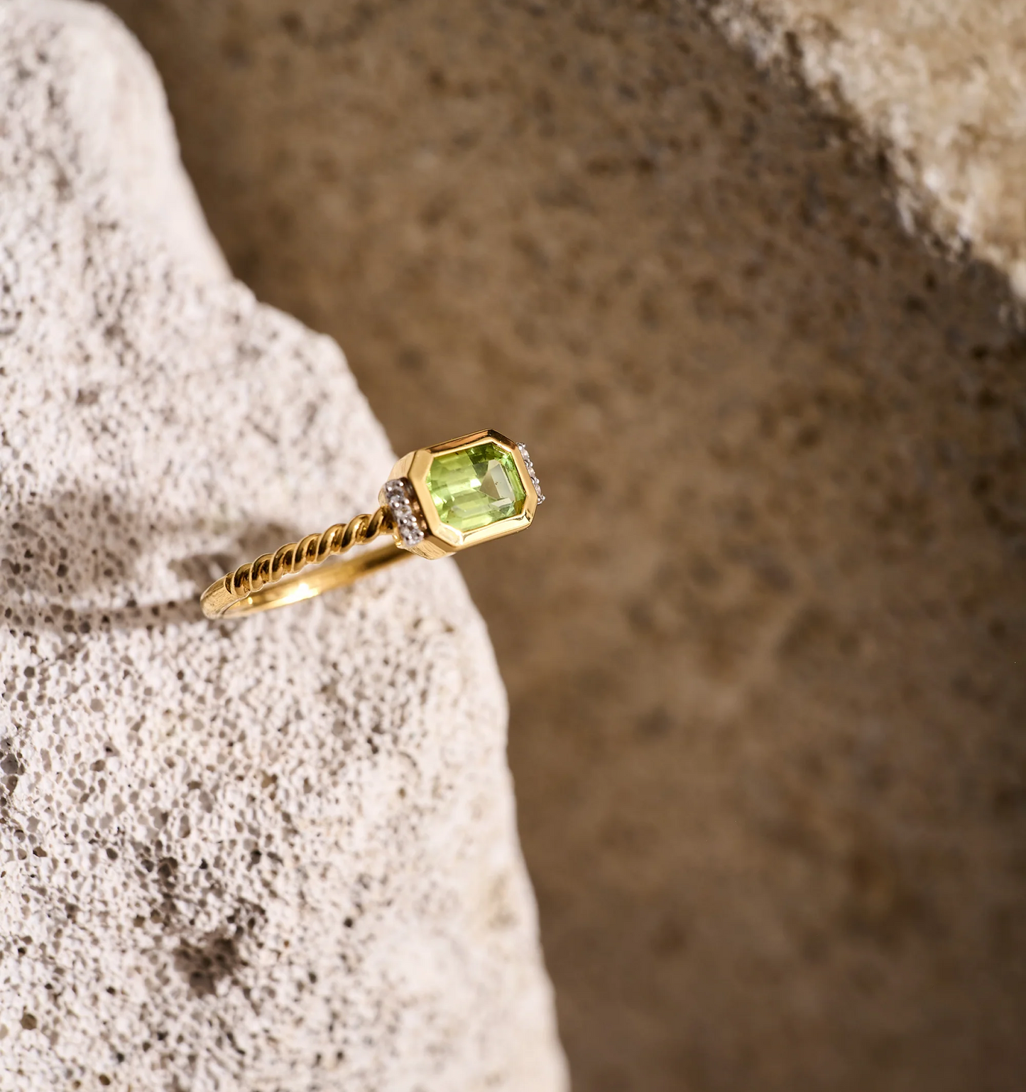 Solae Ring with green peridot and white topaz points on gold band against natural stone background
