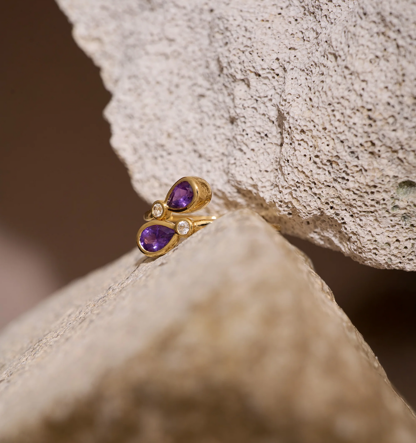 Nimira Ring with twin amethysts and white topaz in gold setting on textured stone background