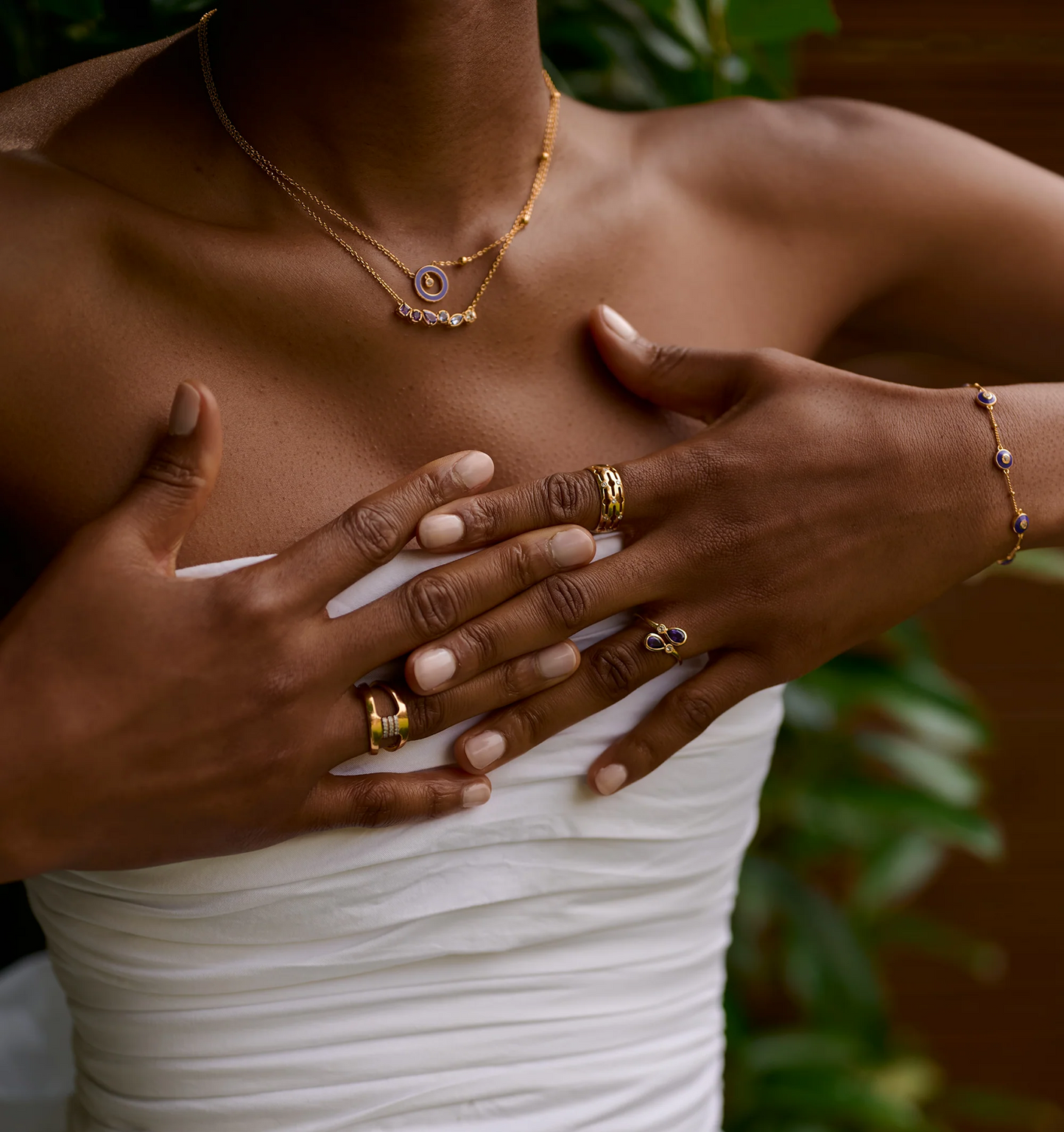 Close-up of hands wearing Nimira Ring with twin amethysts and white topaz gemstones, styled with gold jewelry and white strapless top