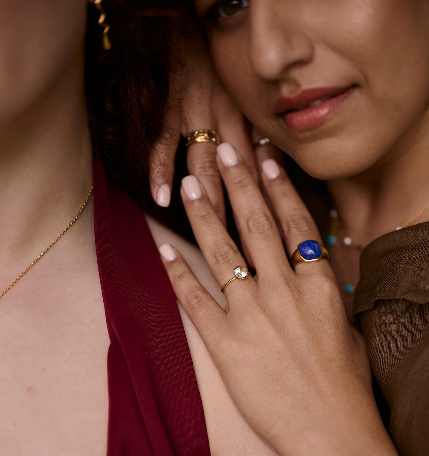 Close-up of two women wearing gold rings, featuring the Neelaya Ring with a bold blue lapis stone on one woman's finger