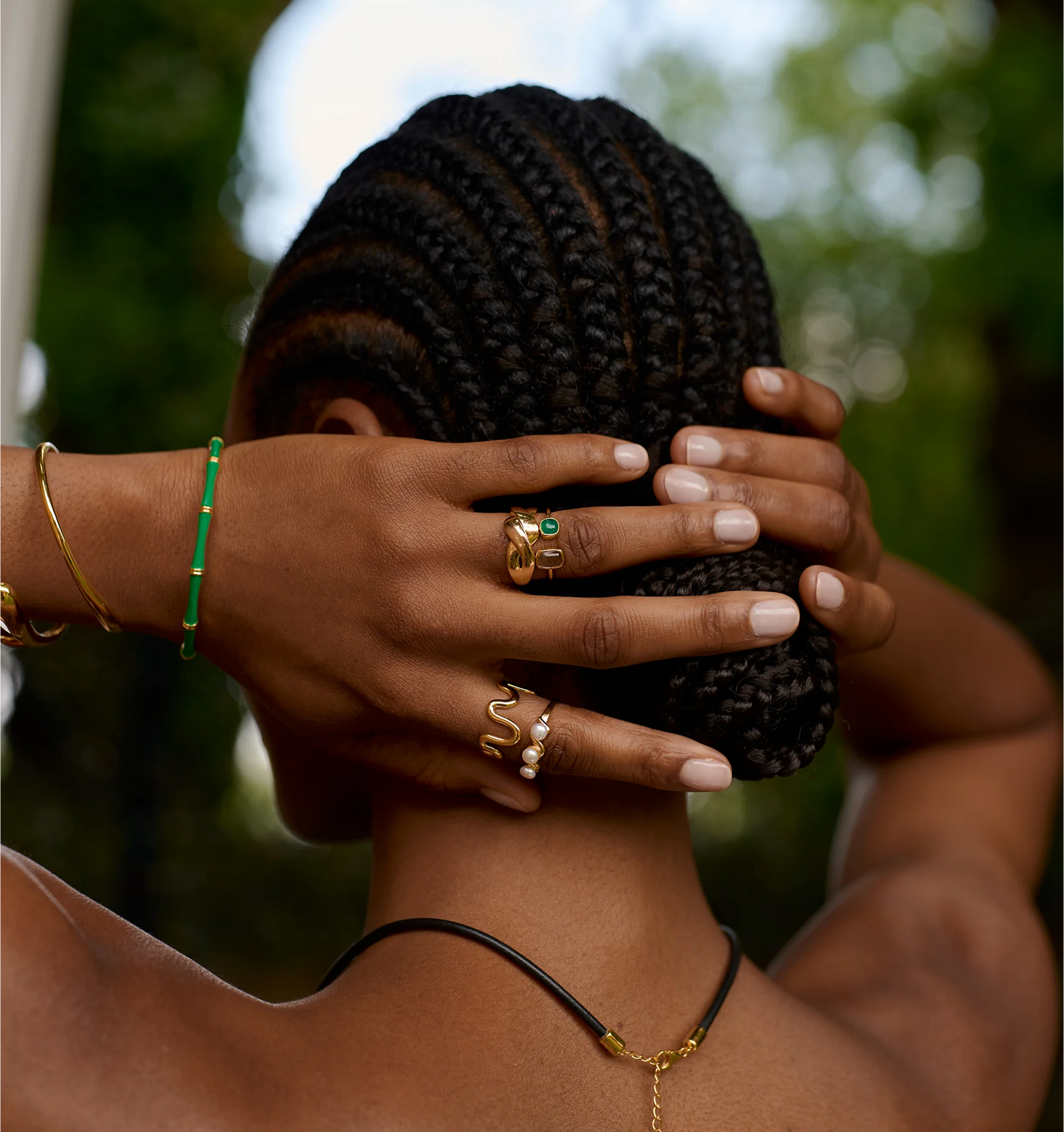 Close-up of hand wearing Tulaa Ring with green onyx and gold detailing on braided hair background
