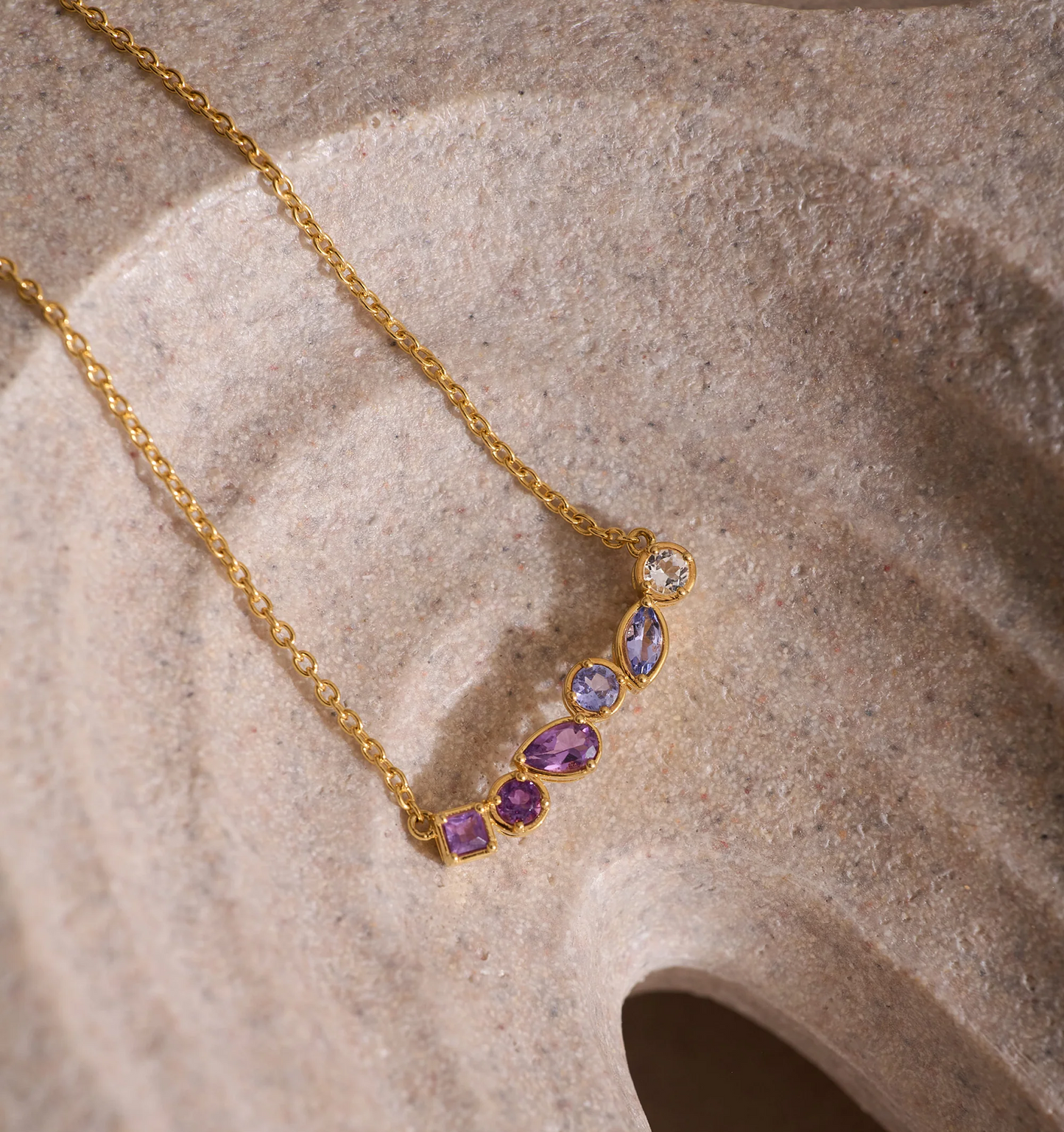 Raag Necklace gold chain with amethyst, tanzanite, and topaz gemstones on textured background