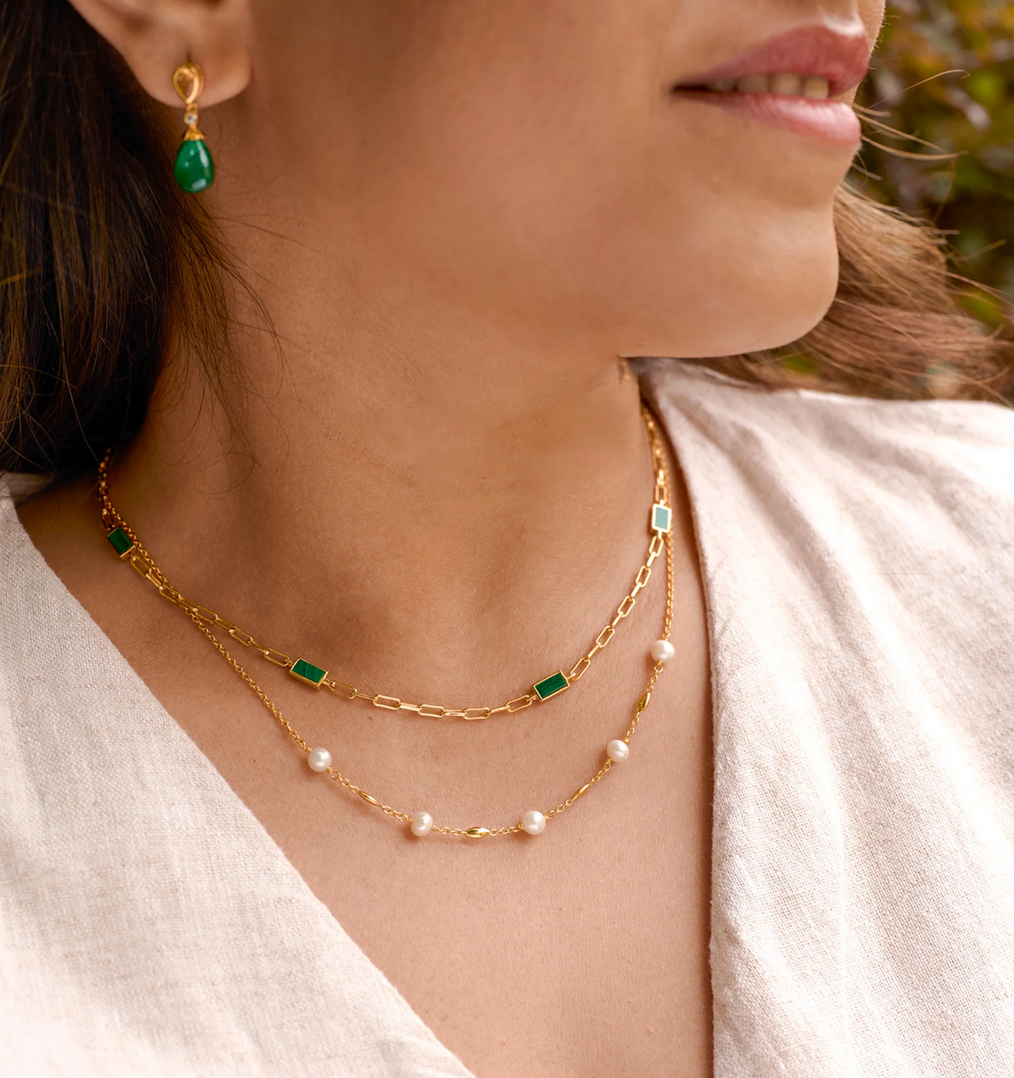 Close-up of a woman wearing the Tarang Necklace with seven malachite stones and pearls on a gold chain, paired with matching green stone earrings.