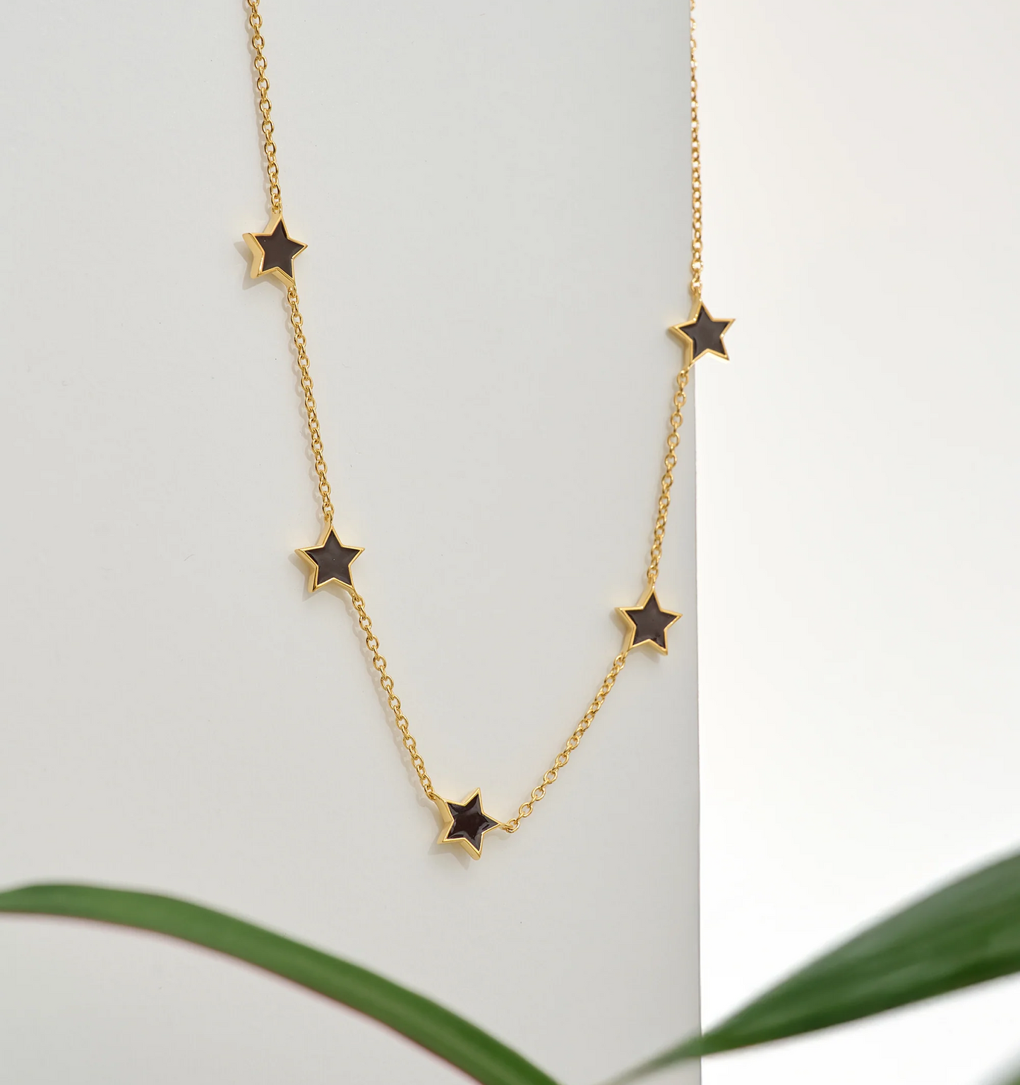 Noctra Necklace gold chain with black star charms on white background
