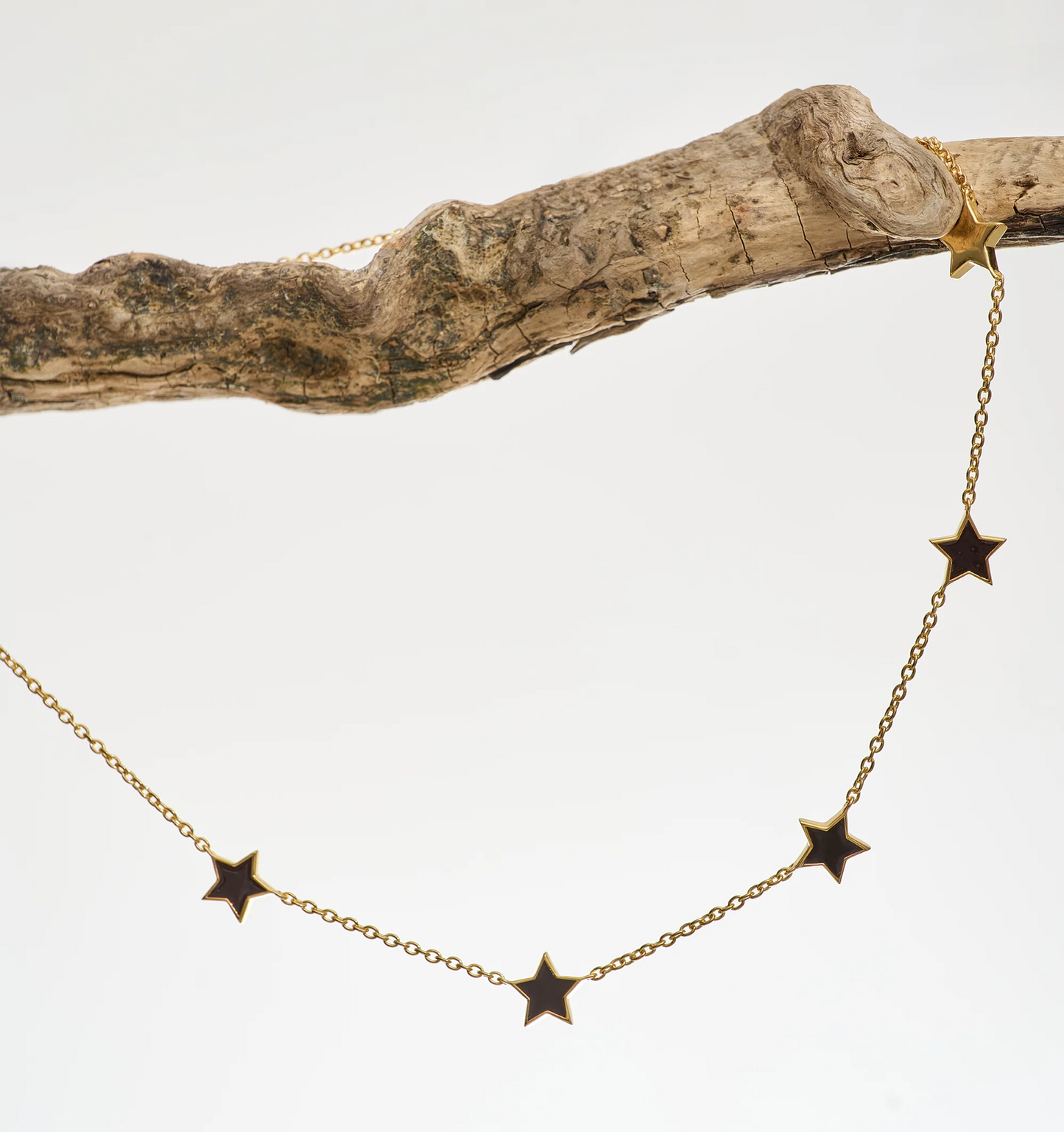 Noctra Necklace gold chain with star-shaped pendants hanging on a rustic branch