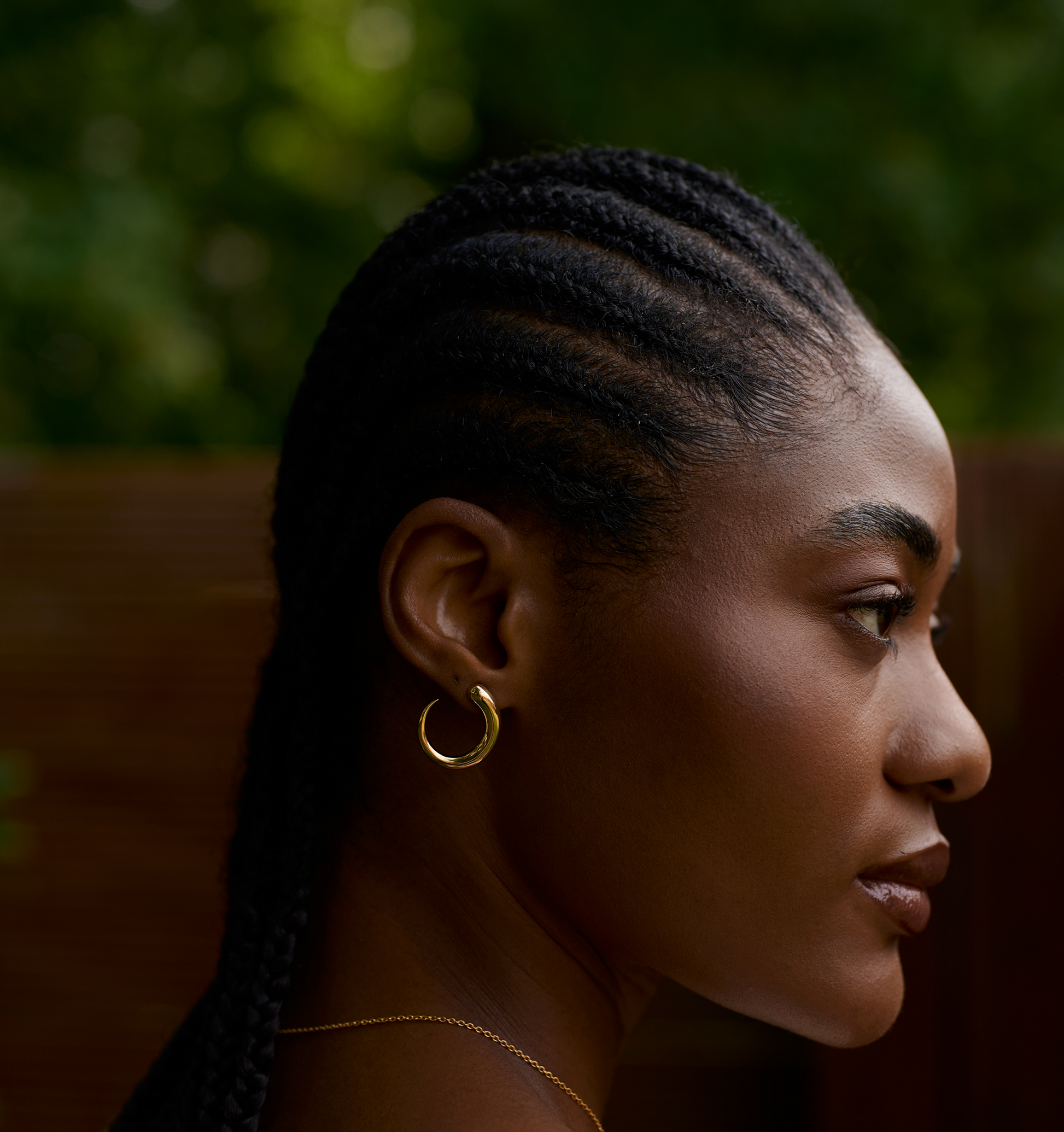 Close-up profile of woman wearing elegant gold Sora earrings with braided hair and natural background