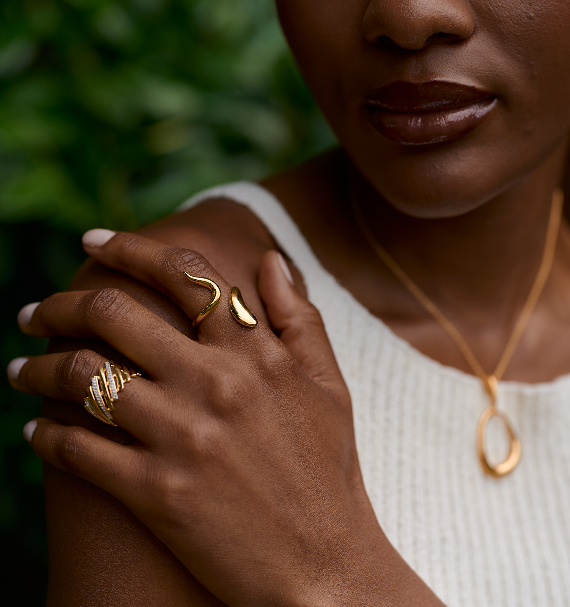 Close-up of a hand wearing a luminous gold Saachi Ring with elegant curved design and complementary gold jewelry.