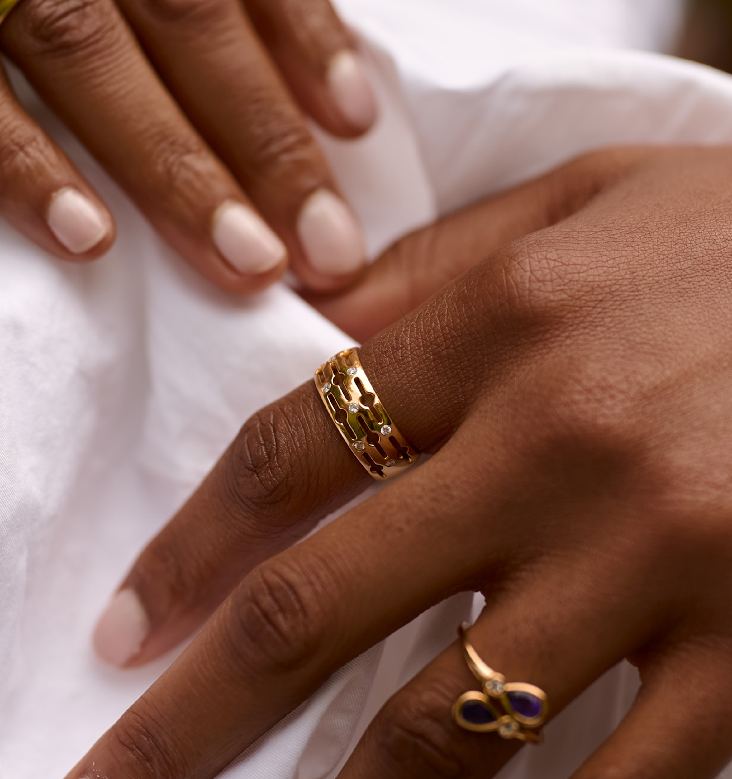 Close-up of a hand wearing a gold Svar Ring with intricate design and diamonds on the finger.