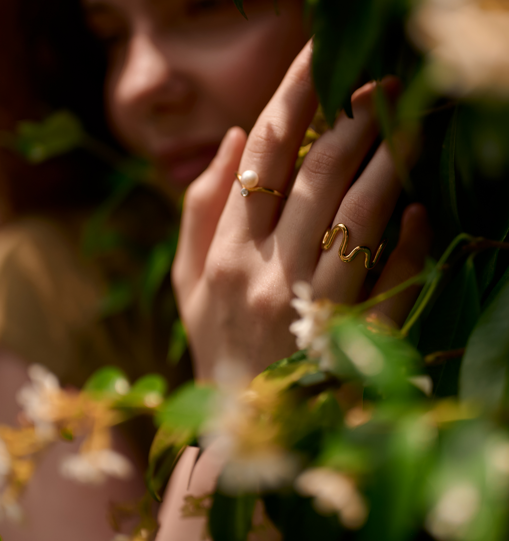 Close-up of hand wearing Sirna Ring with pearl and gold star design among green foliage