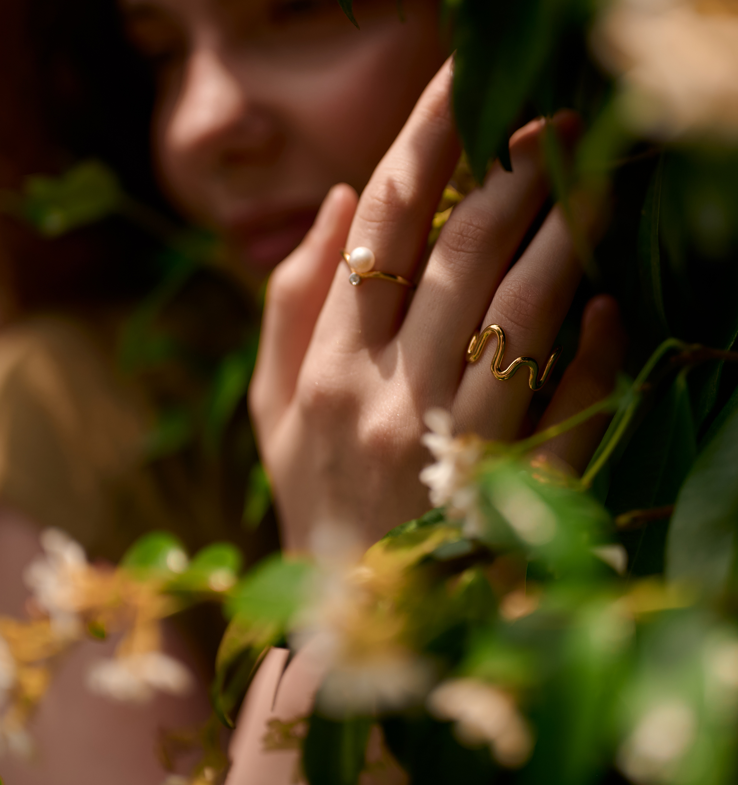 Close-up of hand wearing Sirna Ring with pearl and gold star design among green foliage