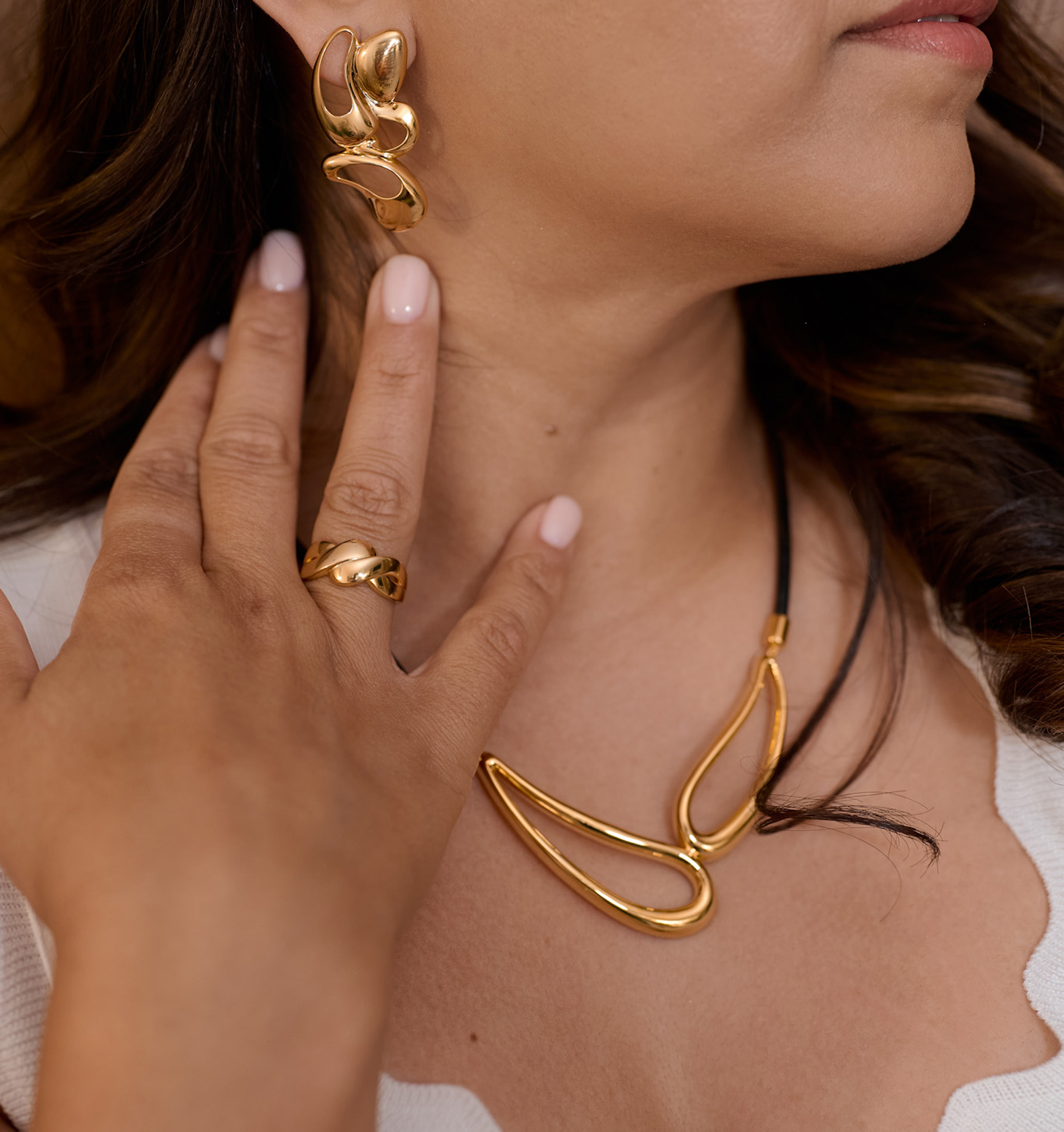 Close-up of a woman's ear wearing radiant gold Nutya earrings with matching gold ring and necklace
