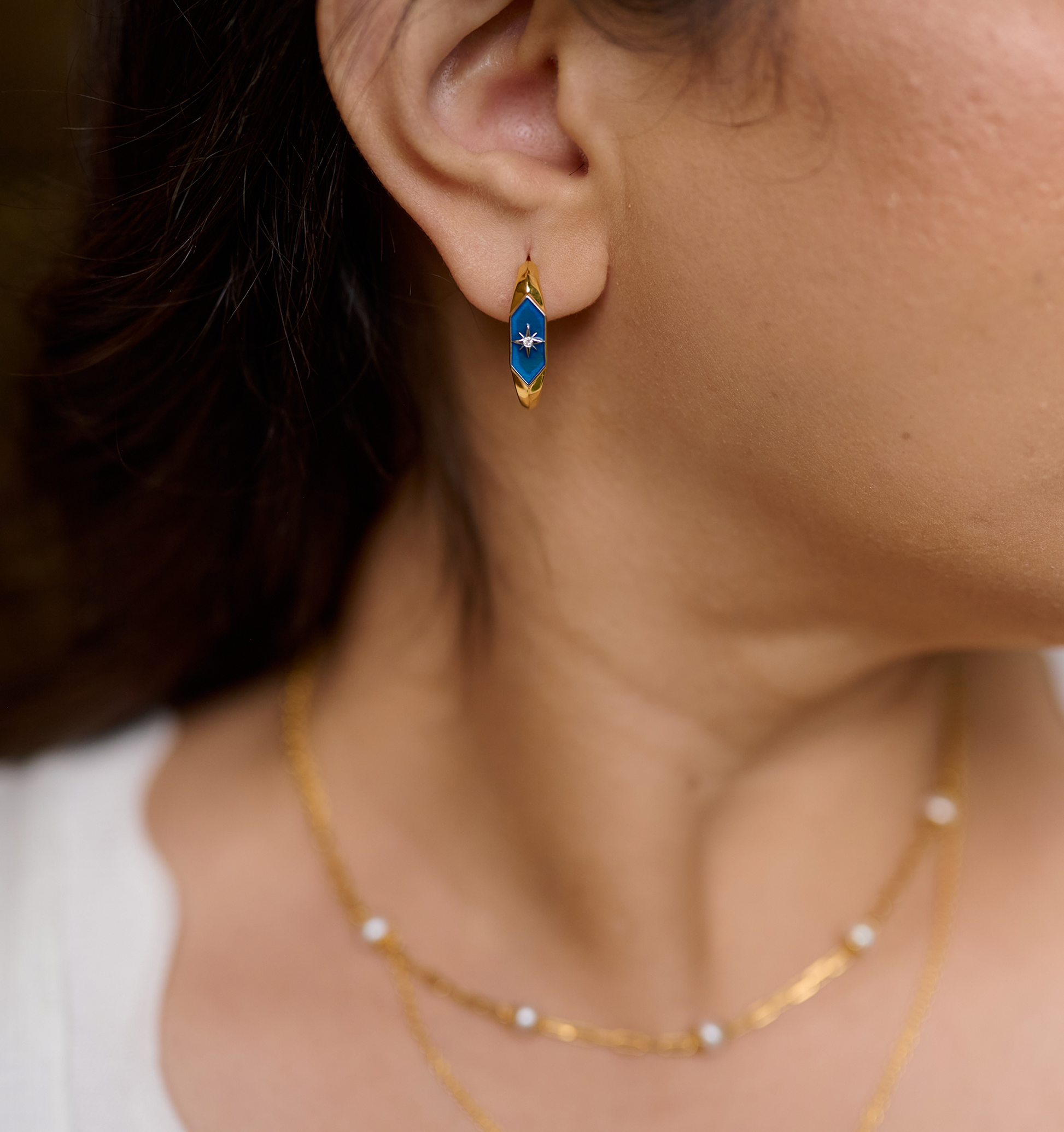 Close-up of ear wearing Lumira Hoops gold earrings with blue star design