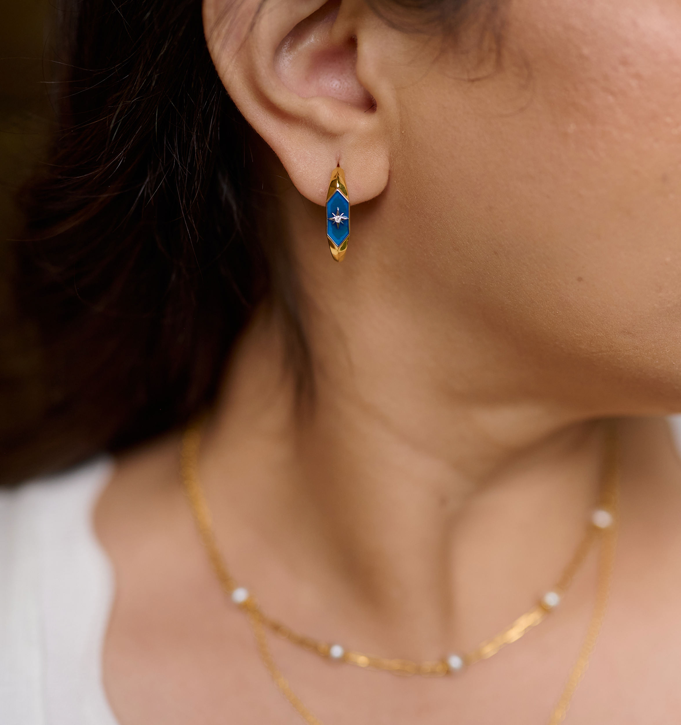 Close-up of ear wearing Lumira Hoops gold earrings with blue star design