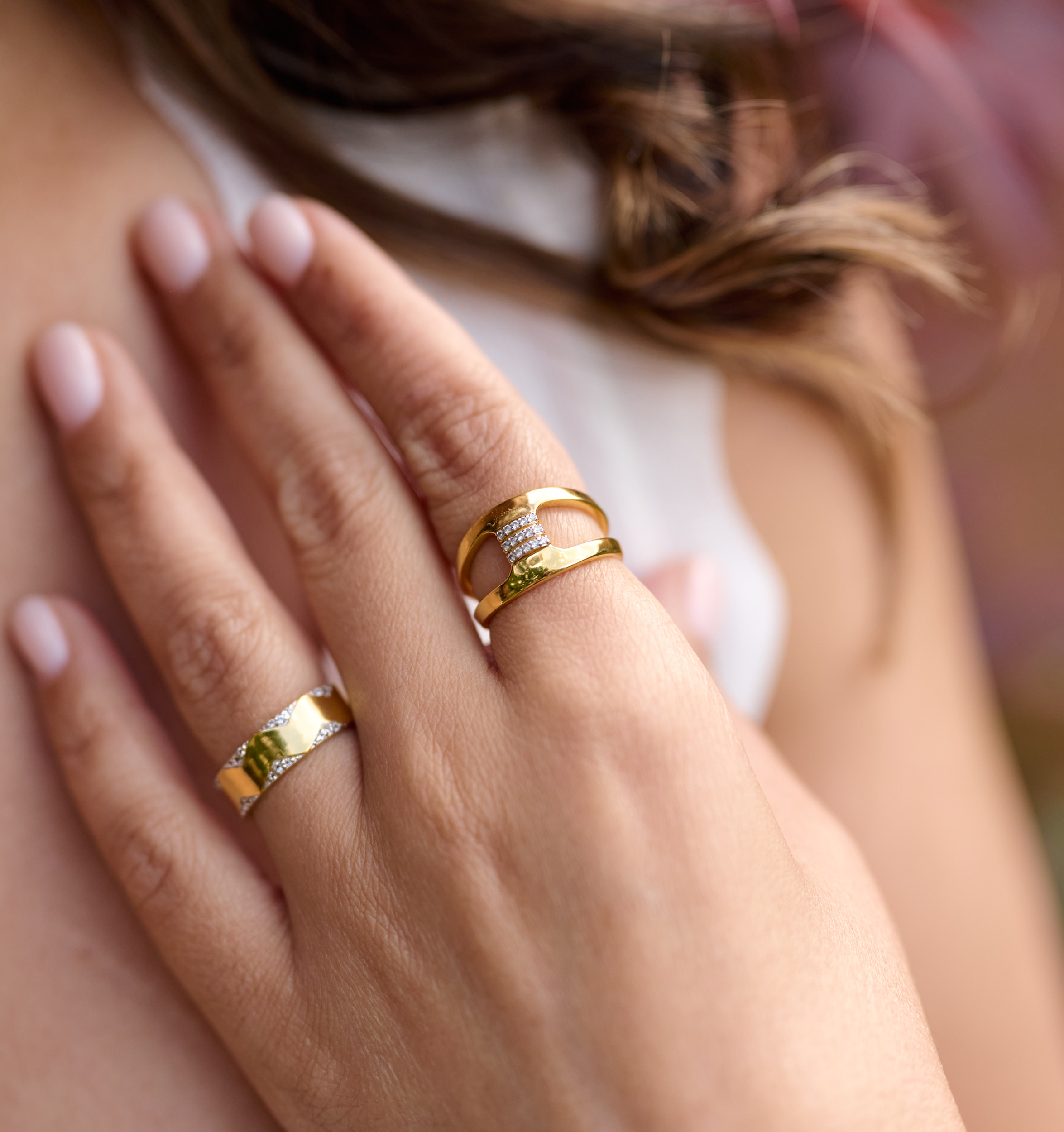 Close-up of hand wearing Setu Ring with two gold arcs connected by white topaz bridge and another gold ring