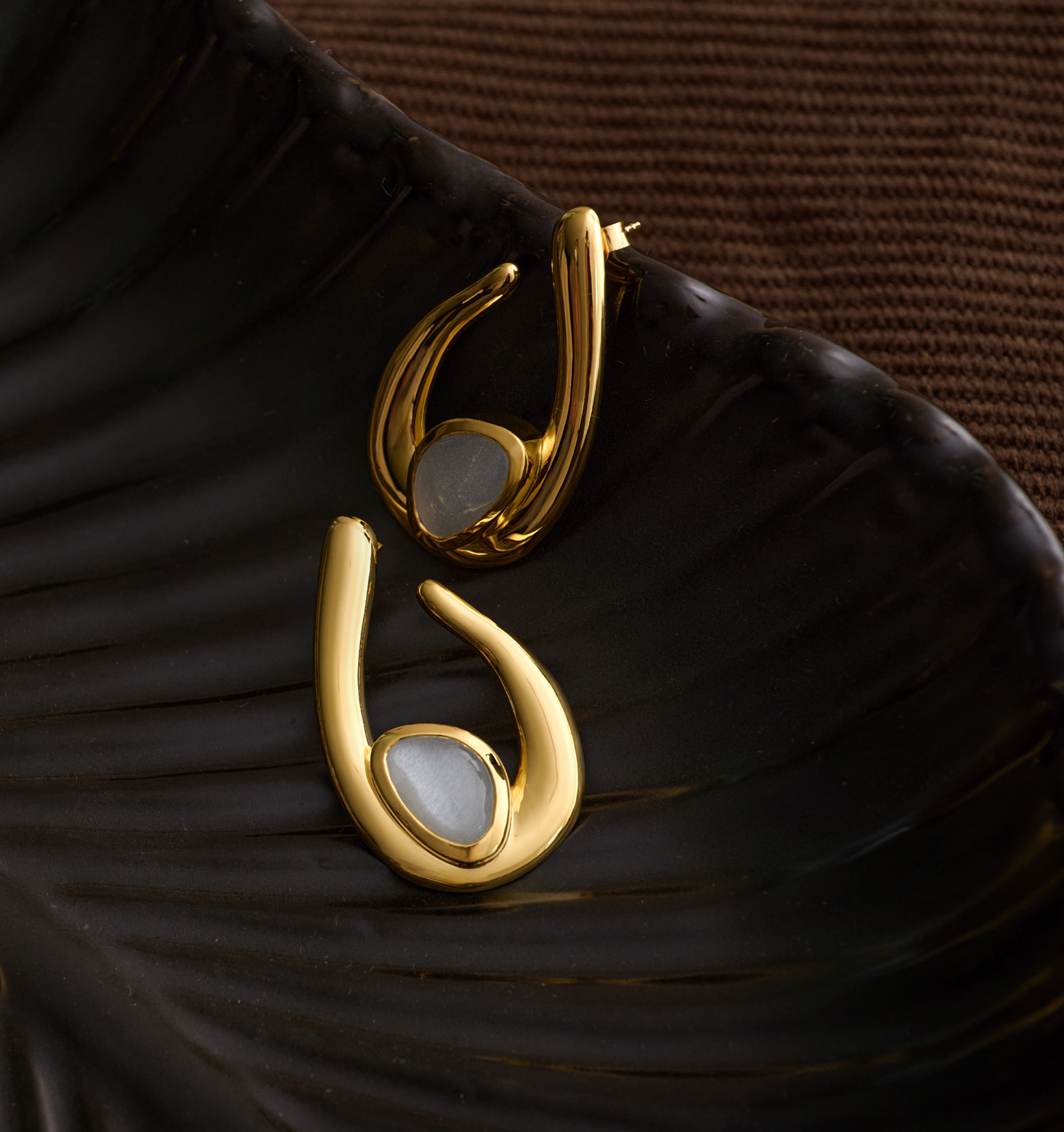 Gold Lunara Earrings with luminous white moonstone on dark textured surface