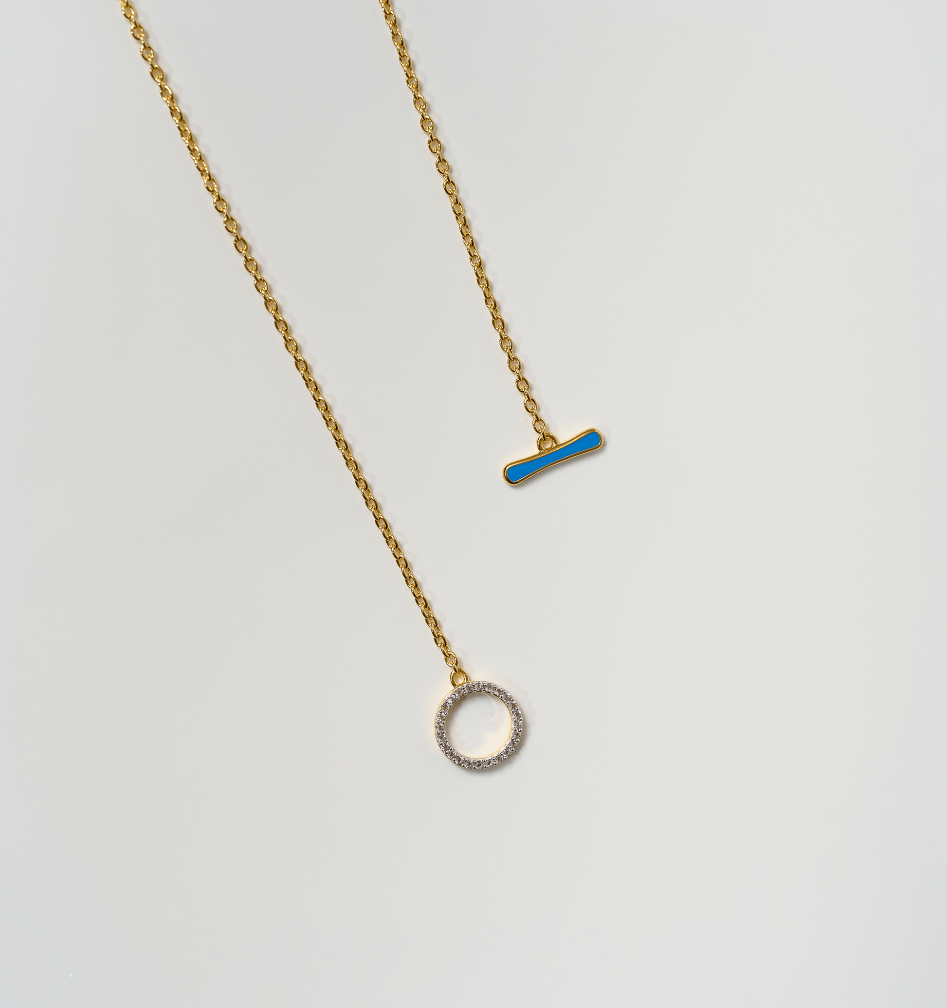 Orya Necklace with white topaz circle and blue bar pendants on gold chains against white background