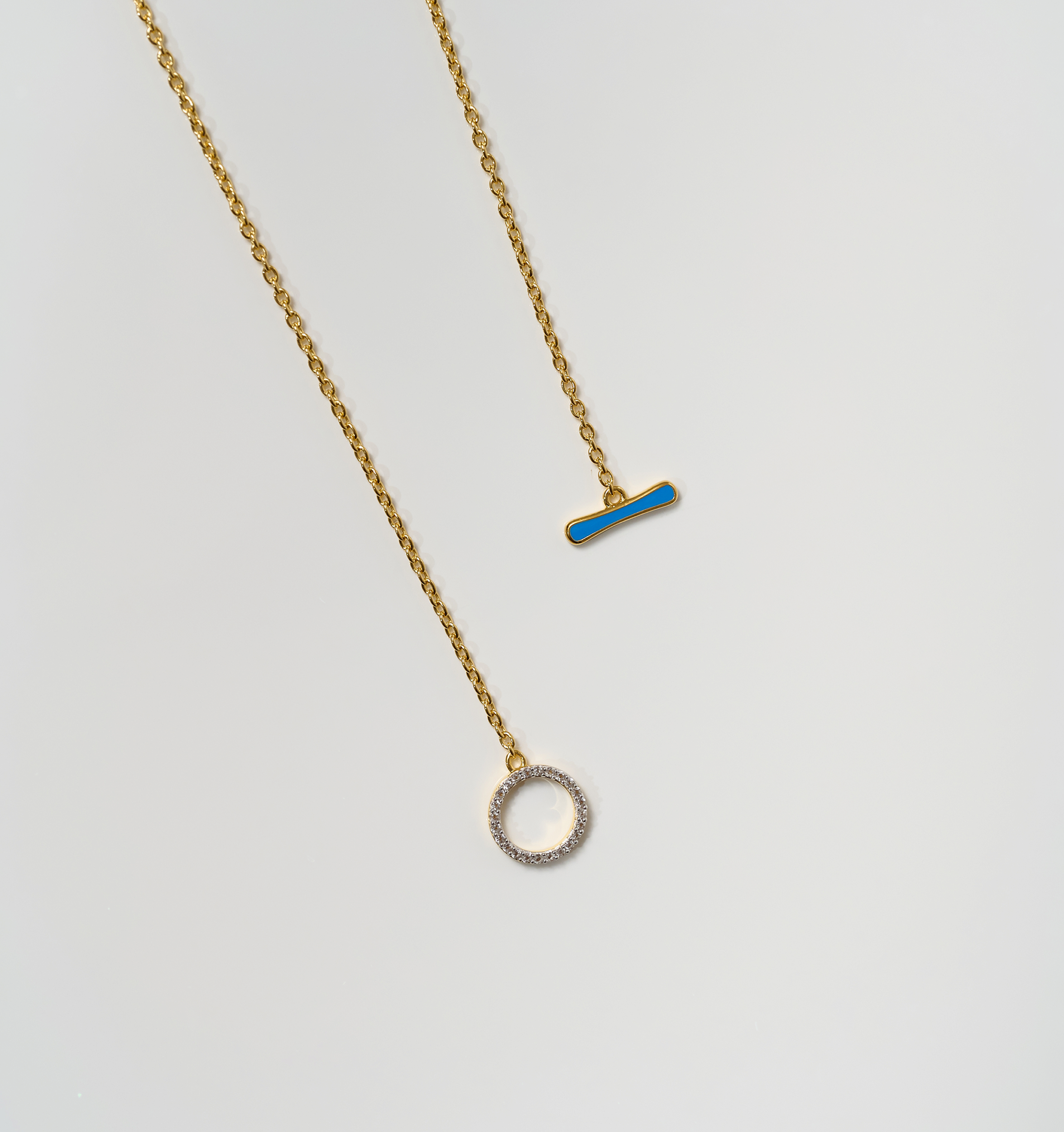 Orya Necklace with white topaz circle and blue bar pendants on gold chains against white background