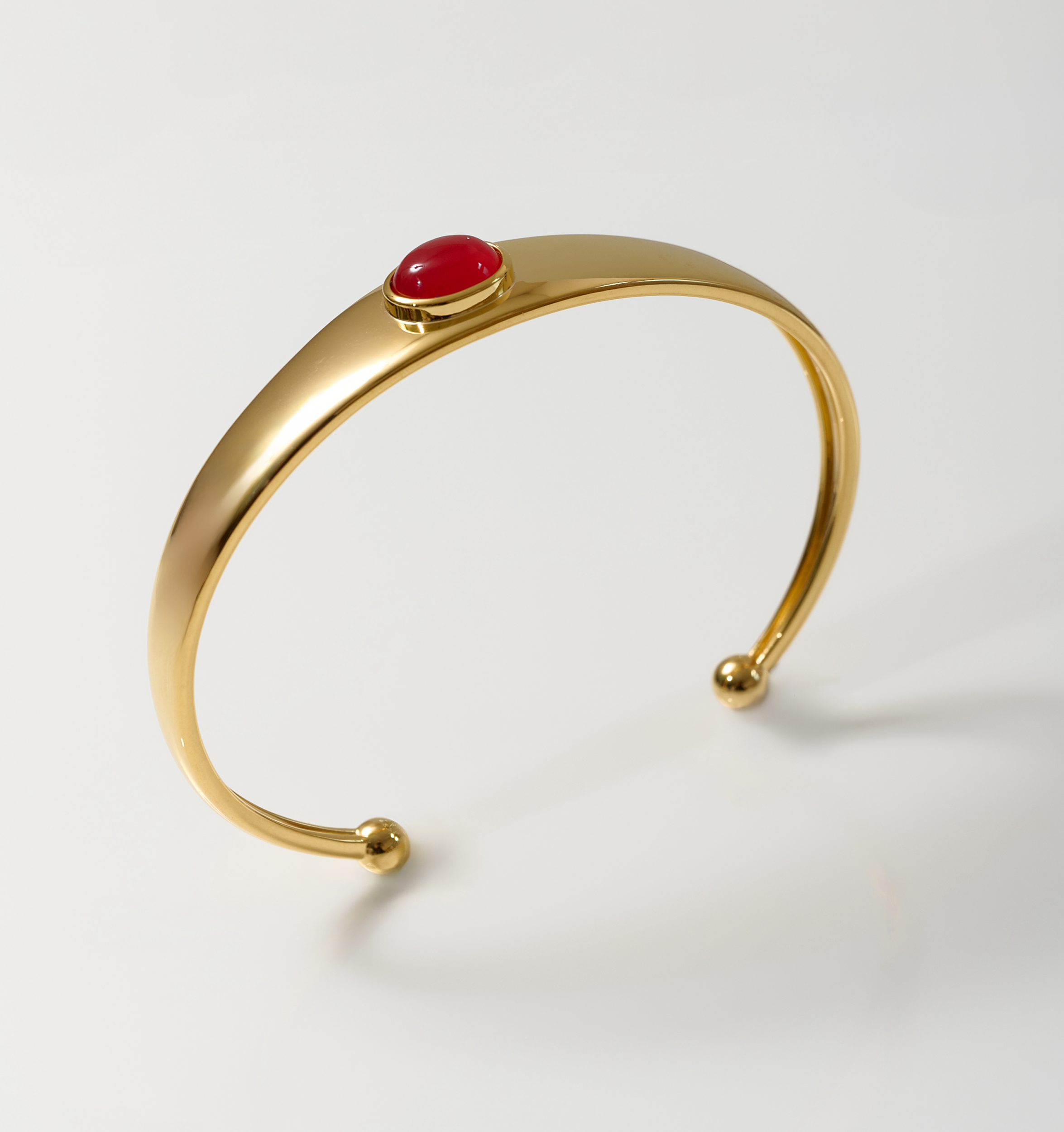 Minimalist gold Dhruva Cuff bracelet with red onyx stone centerpiece on white background