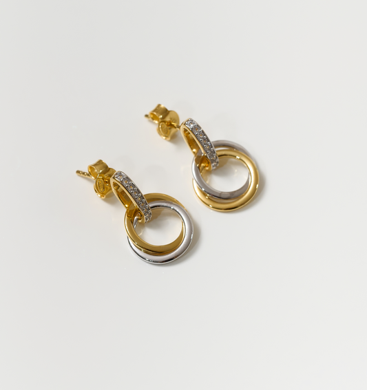 Gold and silver Nirya Earrings with intertwined rings and diamond accents on white background