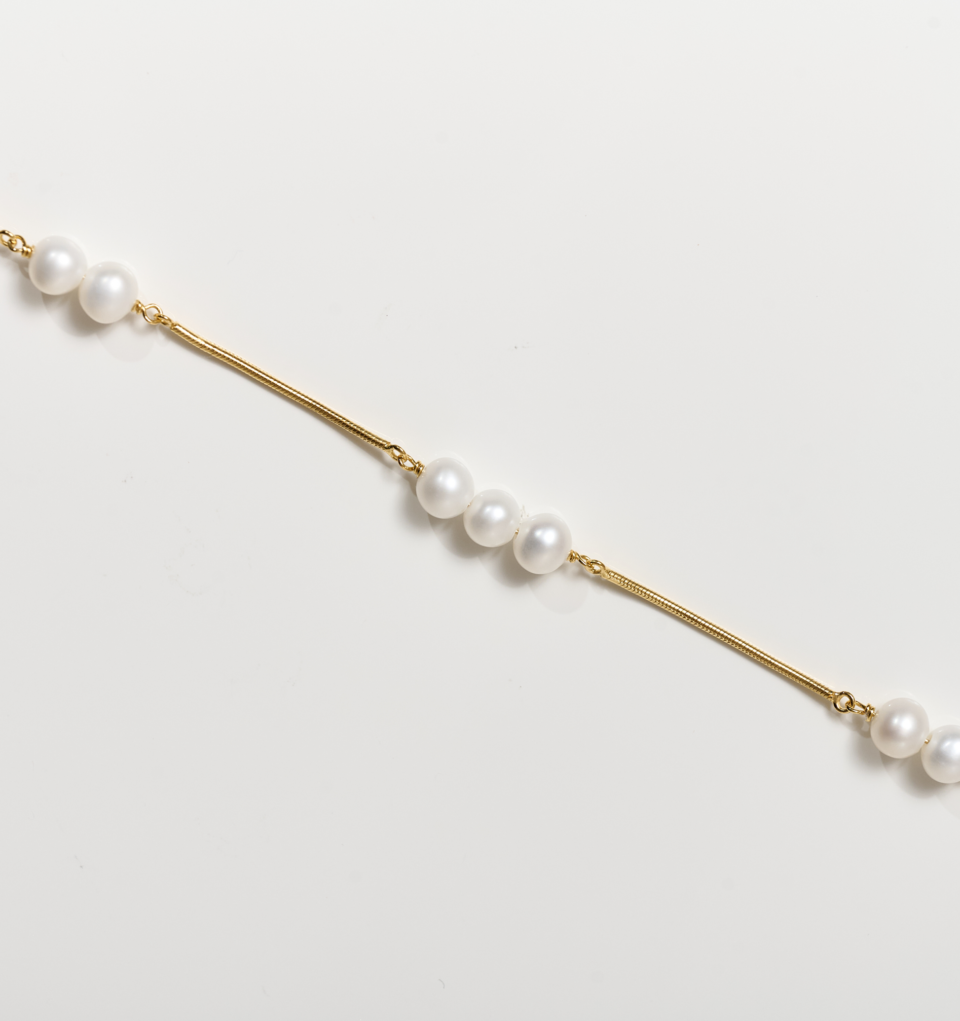 Kanik Bracelet with gold chain and scattered white pearls on white background