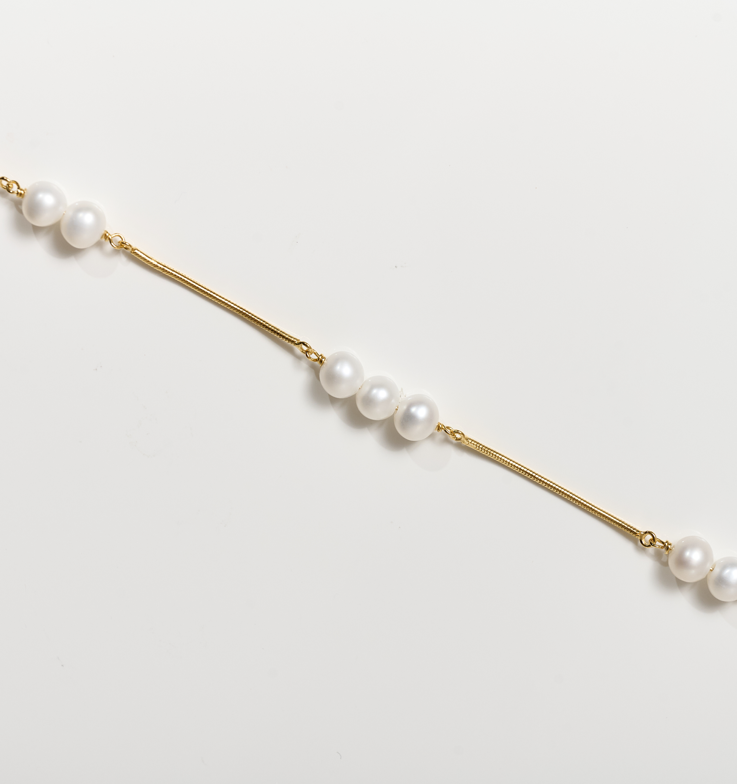 Kanik Bracelet with gold chain and scattered white pearls on white background