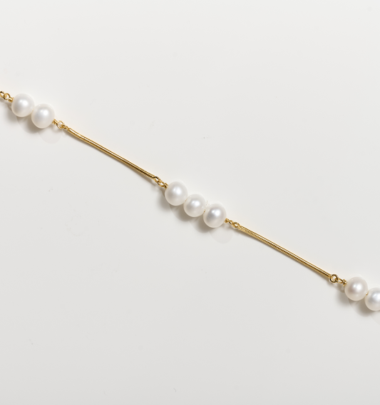 Kanik Bracelet with gold chain and scattered white pearls on white background