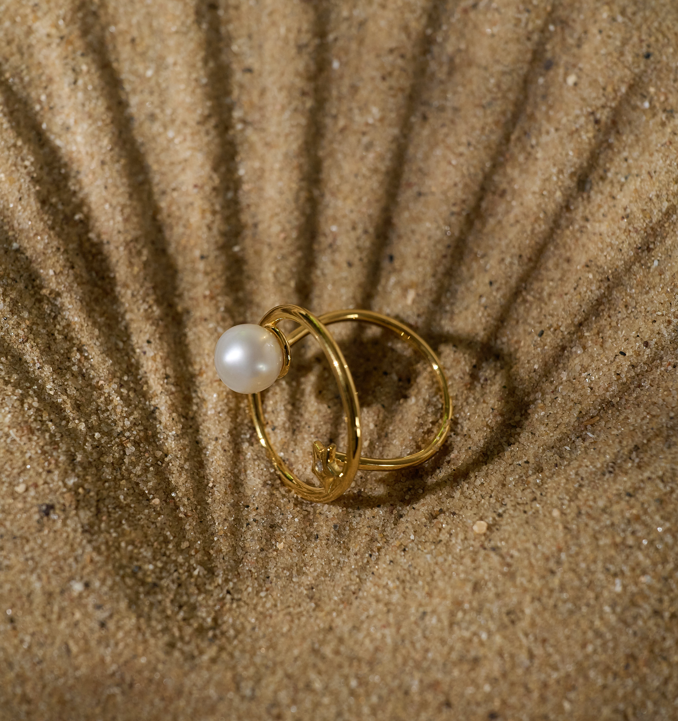 Golden Amishti Ring with pearl and star design on sand background