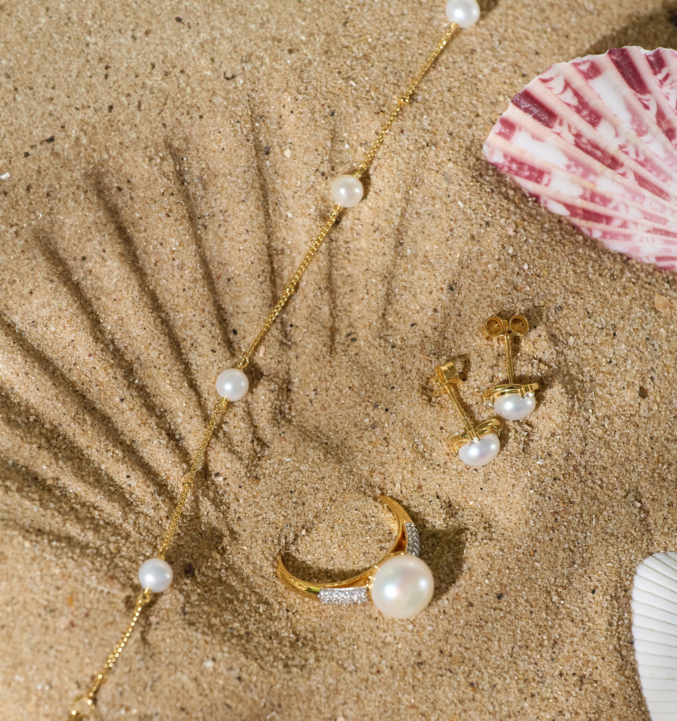 Shanai Bracelet with six pearls on gold chain displayed on sand with matching pearl ring and earrings