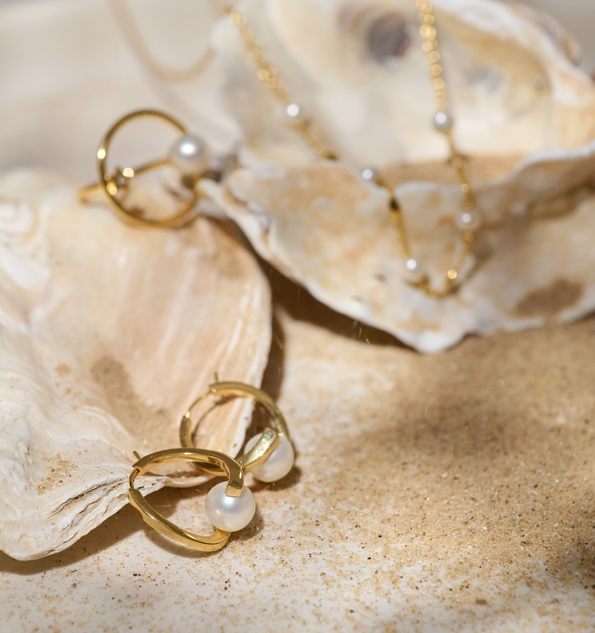 Sharvani Earrings gold hoops with pearls on sandy seashell background