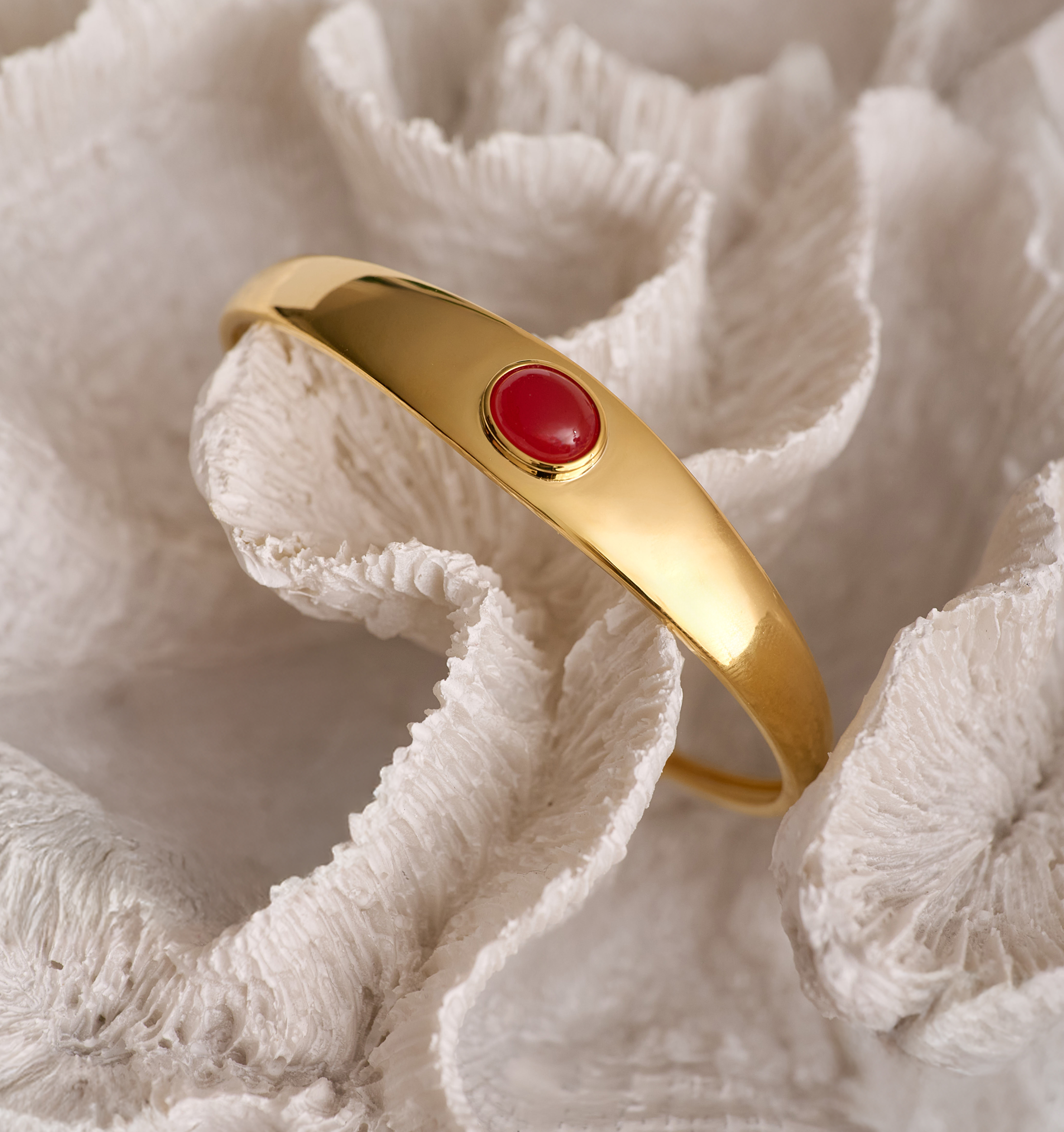 Gold Dhruva Cuff bracelet with red onyx stone on textured white background