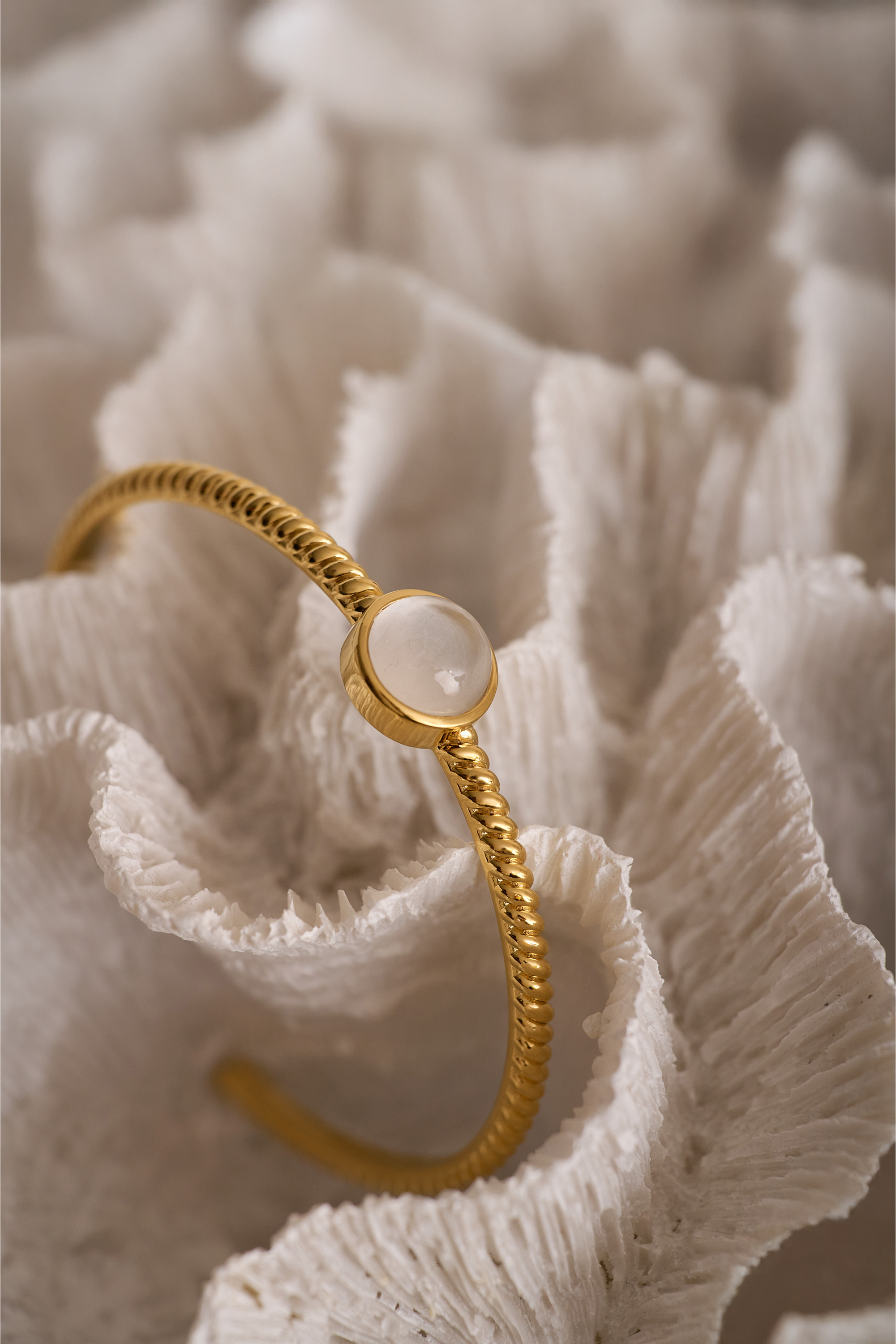 Gold Tarini Cuff bracelet with moonstone talisman on textured fabric background