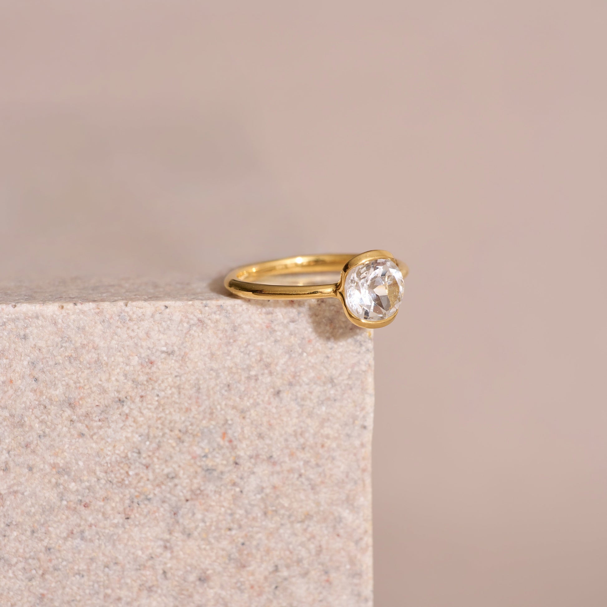 Ruhi Ring with delicate white topaz set in polished gold band on stone surface