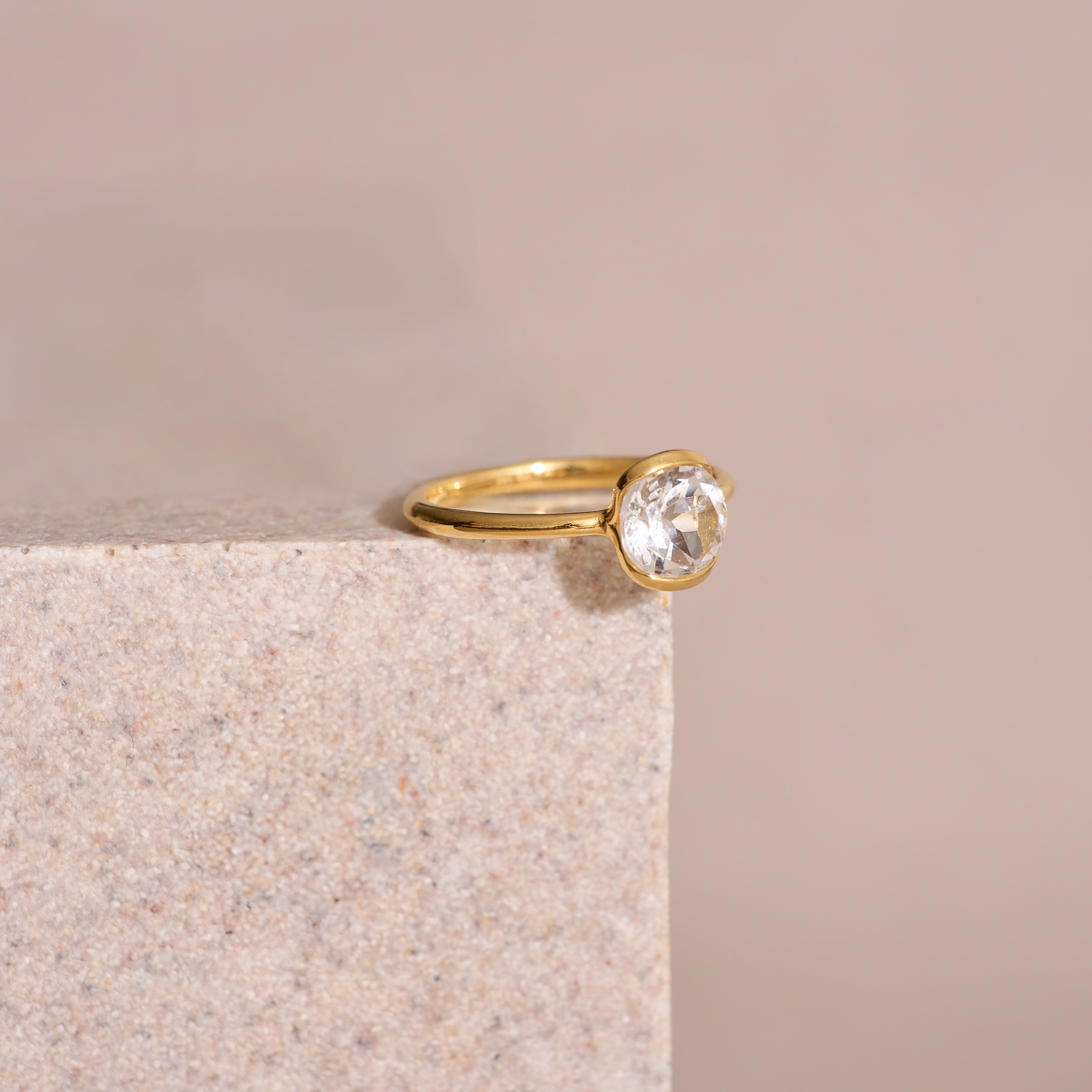 Ruhi Ring with delicate white topaz set in polished gold band on stone surface