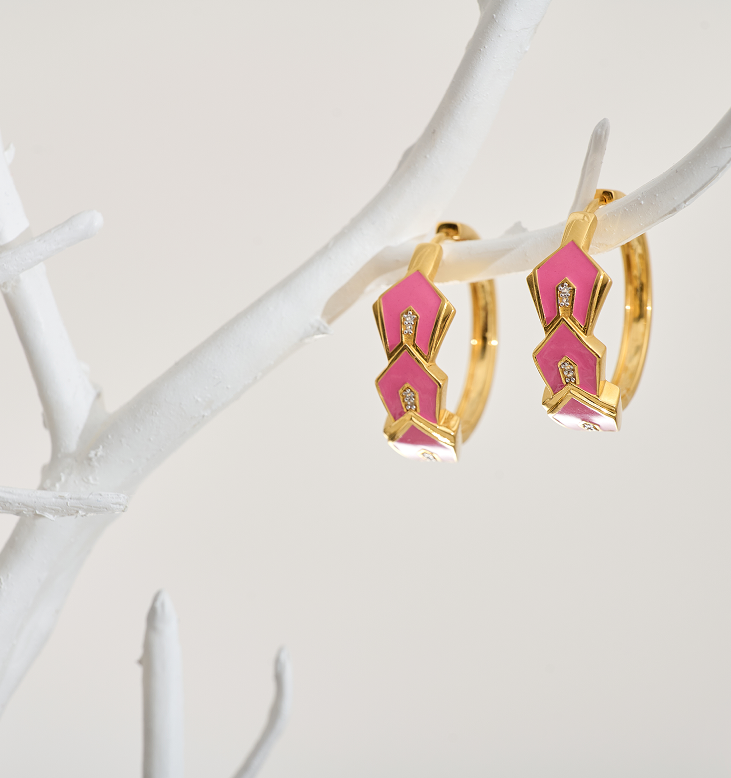Gulzar Petal Dew gold-plated hoops with pink enamel petals and white topaz accents hanging on white branch