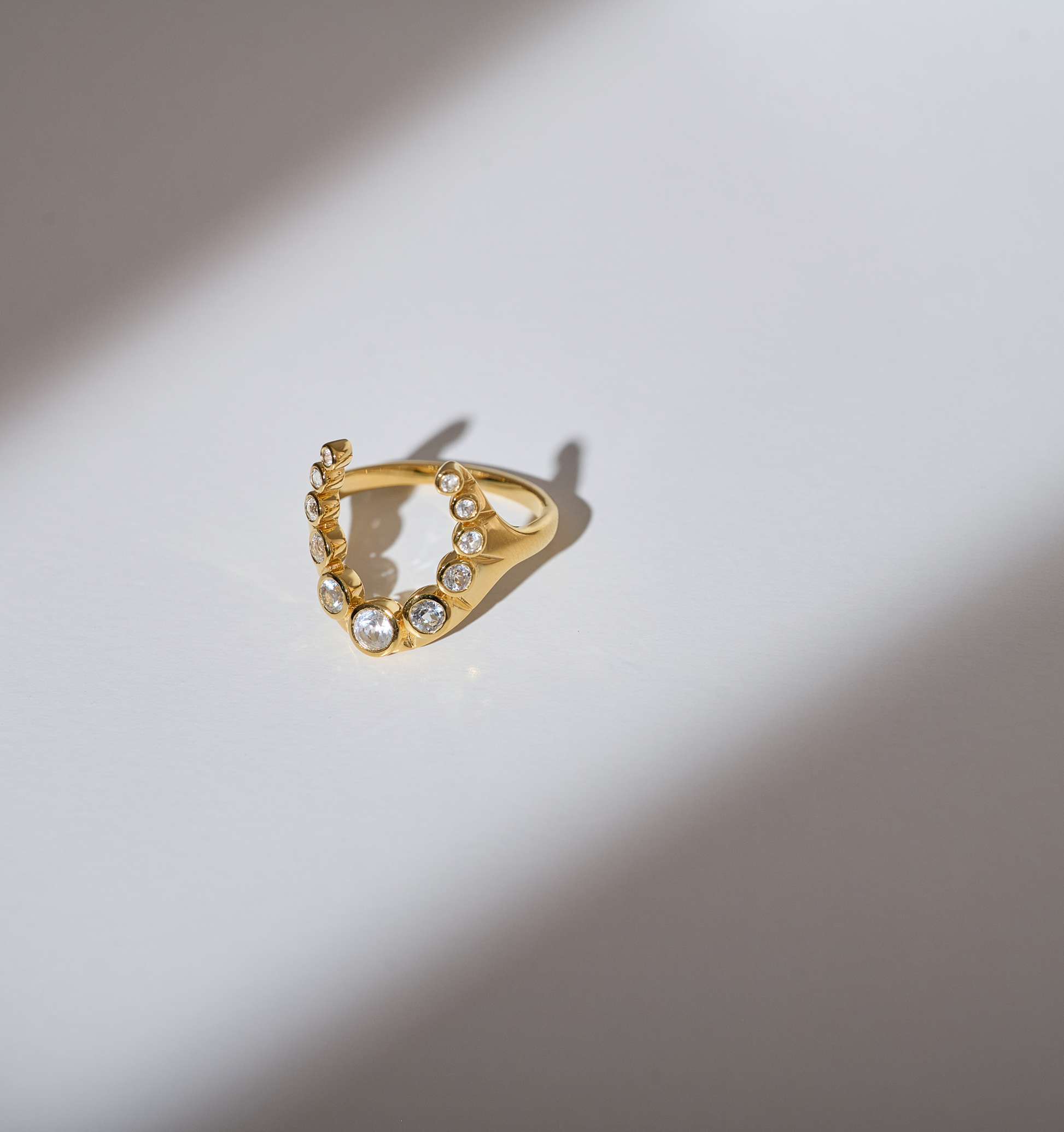 Gold Rakira ring with 11 white topaz stones in a crescent shape on a white surface