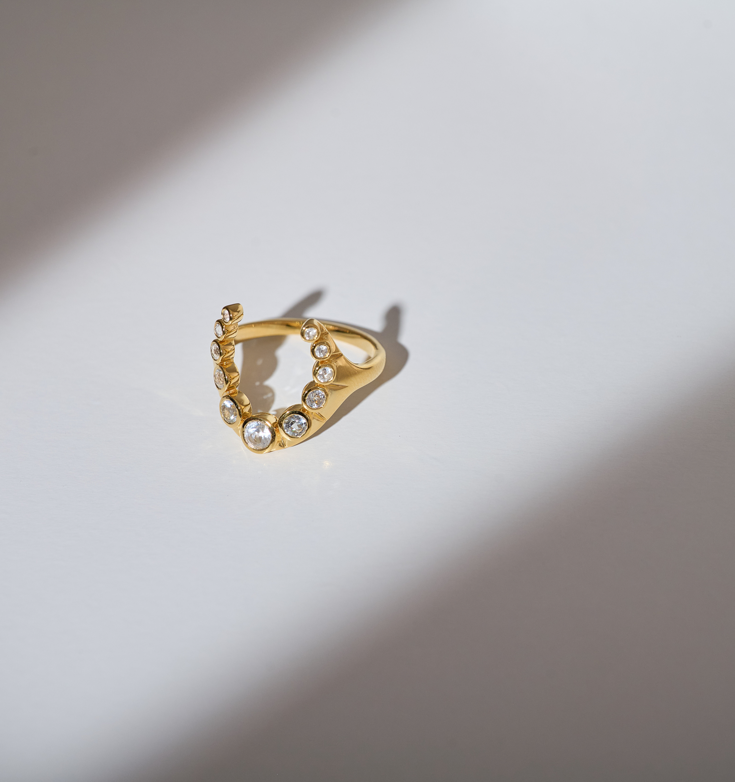 Gold Rakira ring with 11 white topaz stones in a crescent shape on a white surface