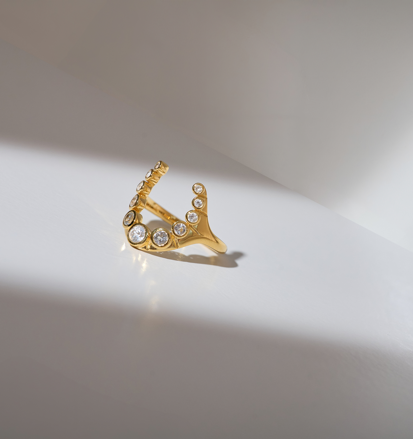 Gold Rakira Ring with 11 white topaz gemstones in horseshoe shape on neutral background