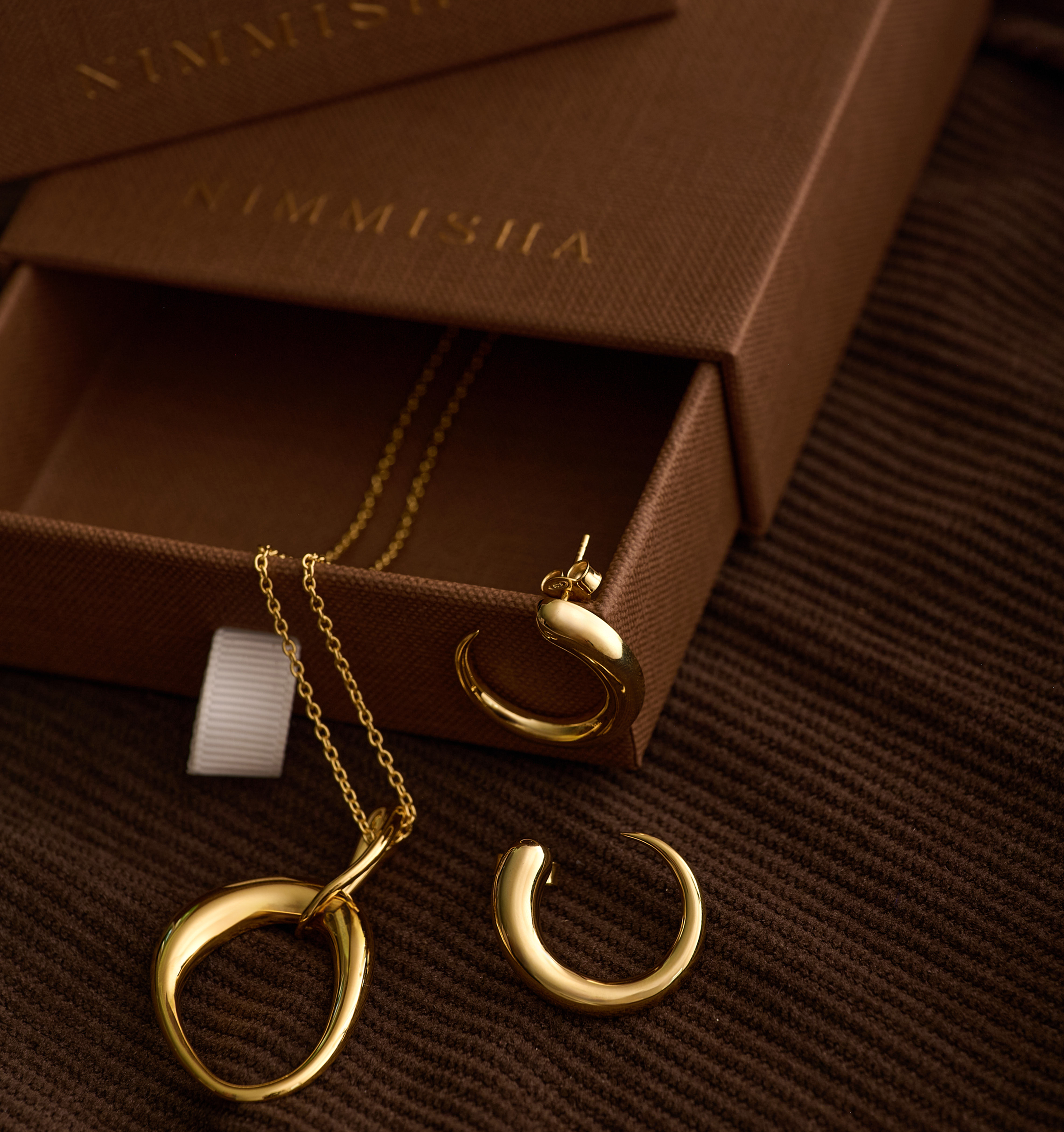 Bindu Necklace sculpted gold drop pendant with matching gold earrings on brown textured background