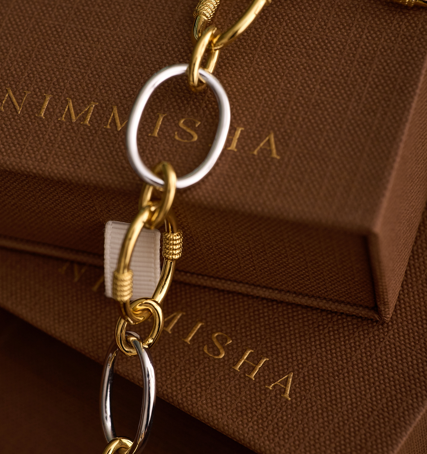 Close-up of Tasya Necklace with intertwined gold and silver links on brown textured boxes